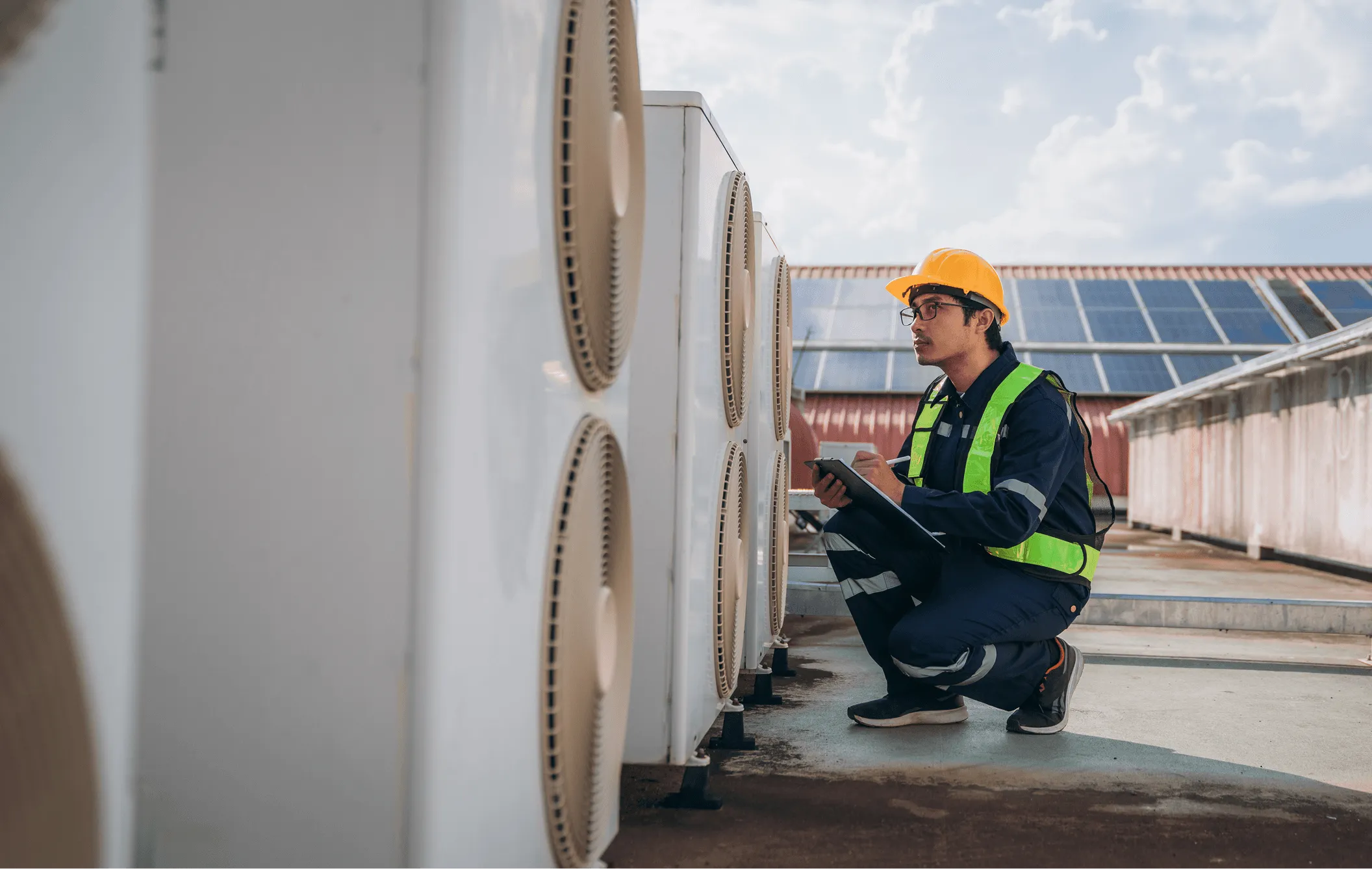 Technicien effectuant l’entretien d’unités de climatisation extérieures sur un toit résidentiel.