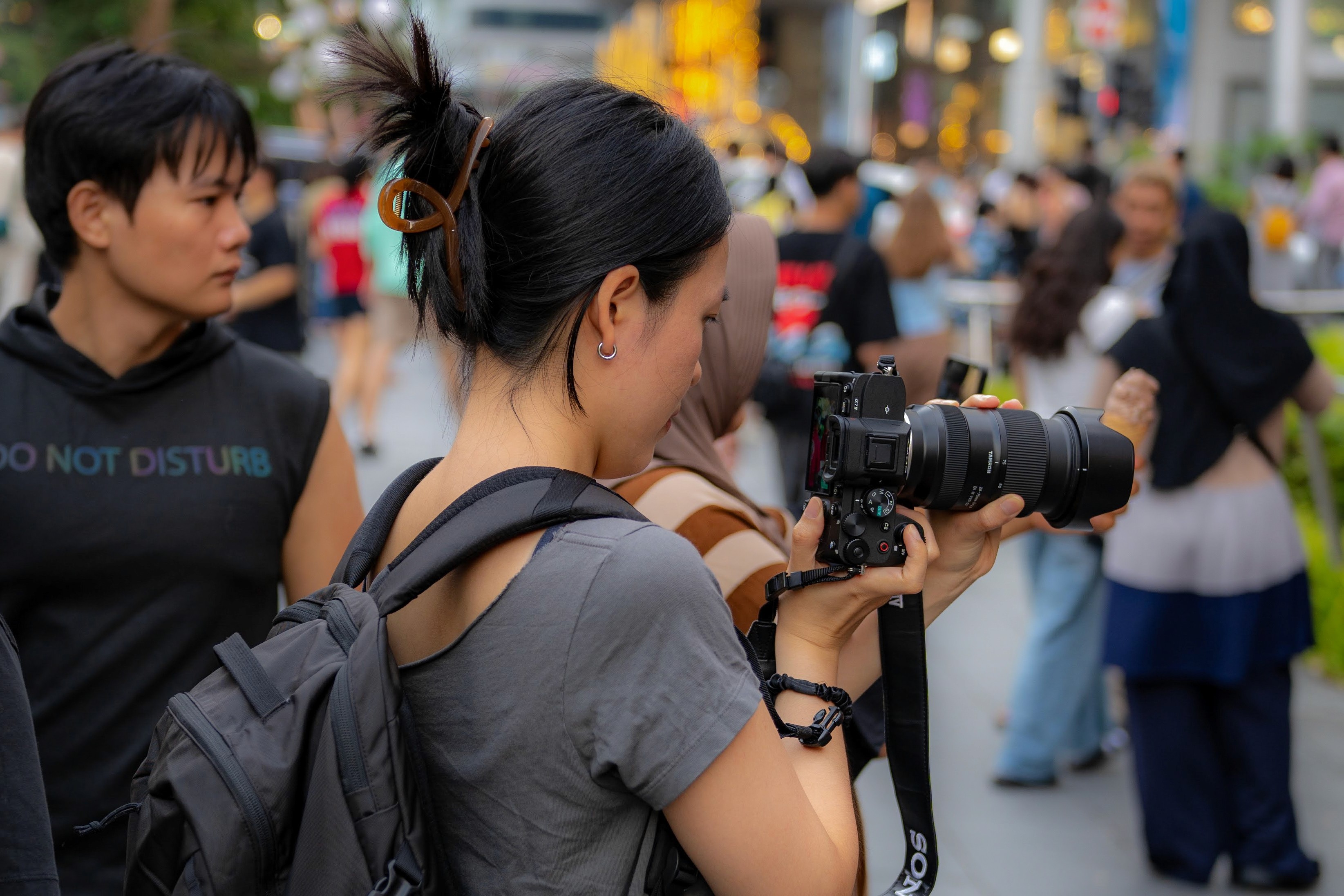 A woman named Grace looking into the screen of her camera in a crowded outdoor space