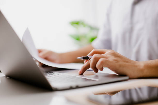 Close-up of hands holding a pen while working at a laptop
