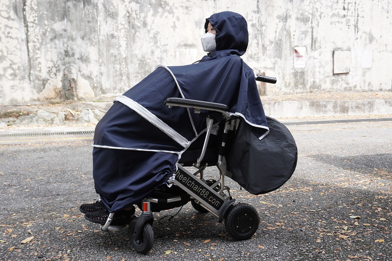 Side view of a wheelchair user seated on a wheelchair outdoors, wearing the 55 Minutes Wheelchair Poncho