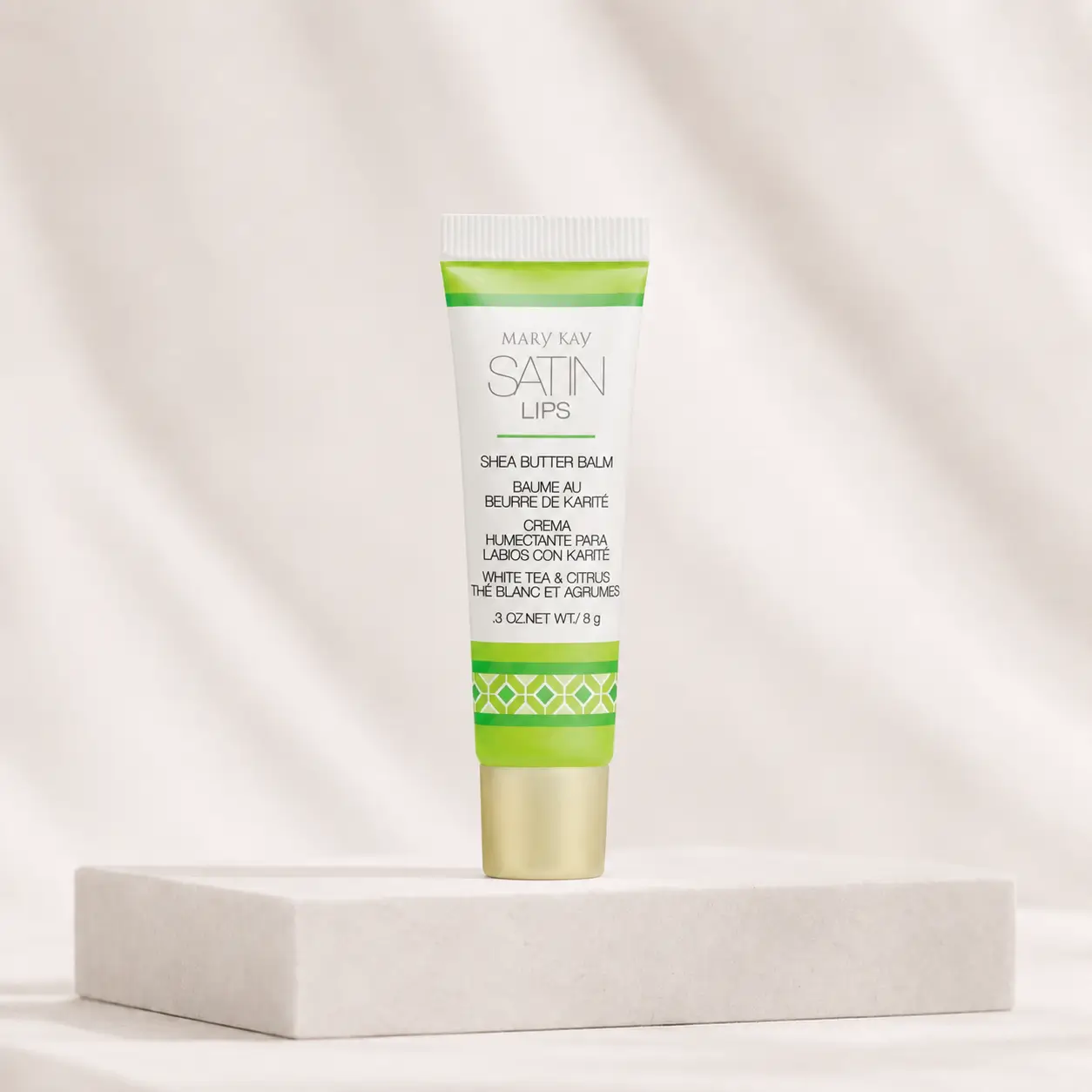 Bálsamo para os Lábios Satin Lips Karité Aroma de Chá Branco & Citrus Mary Kay, em embalagem branca e verde sobre pedestal claro