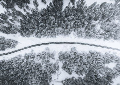 Aerial winter landscape with icy roadway cutting through snowy trees.
