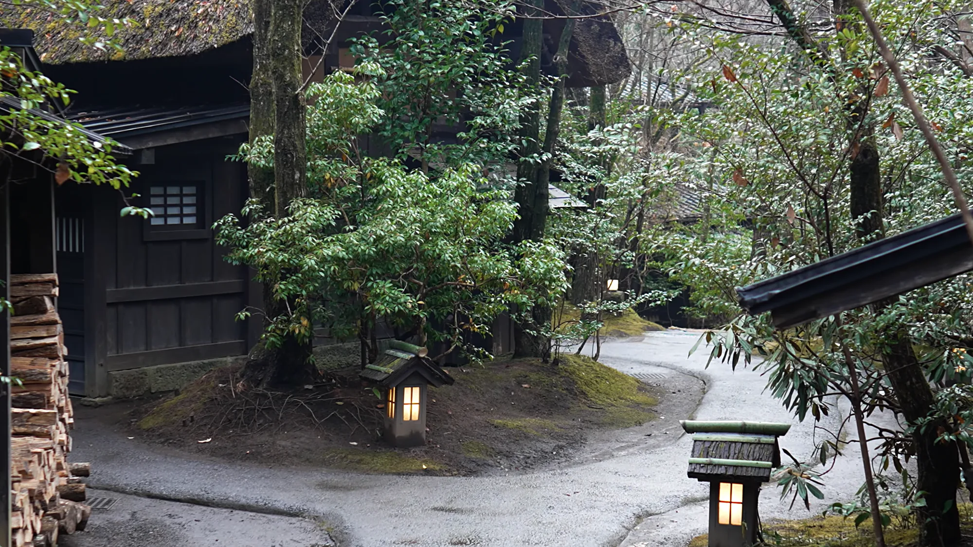 Inn grounds at Kurokawa Onsen with a gravel path, a stone lantern and a stack of firewood