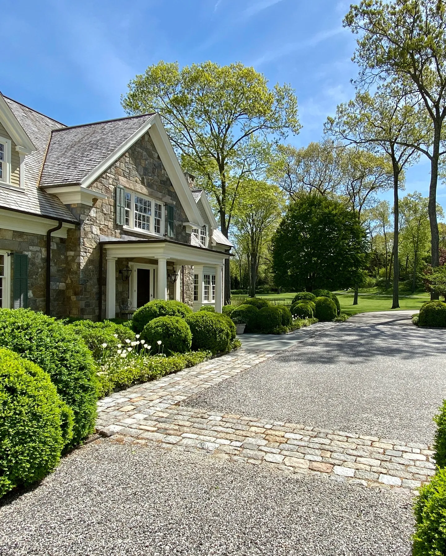 A large house with a driveway and lush greenery in front.