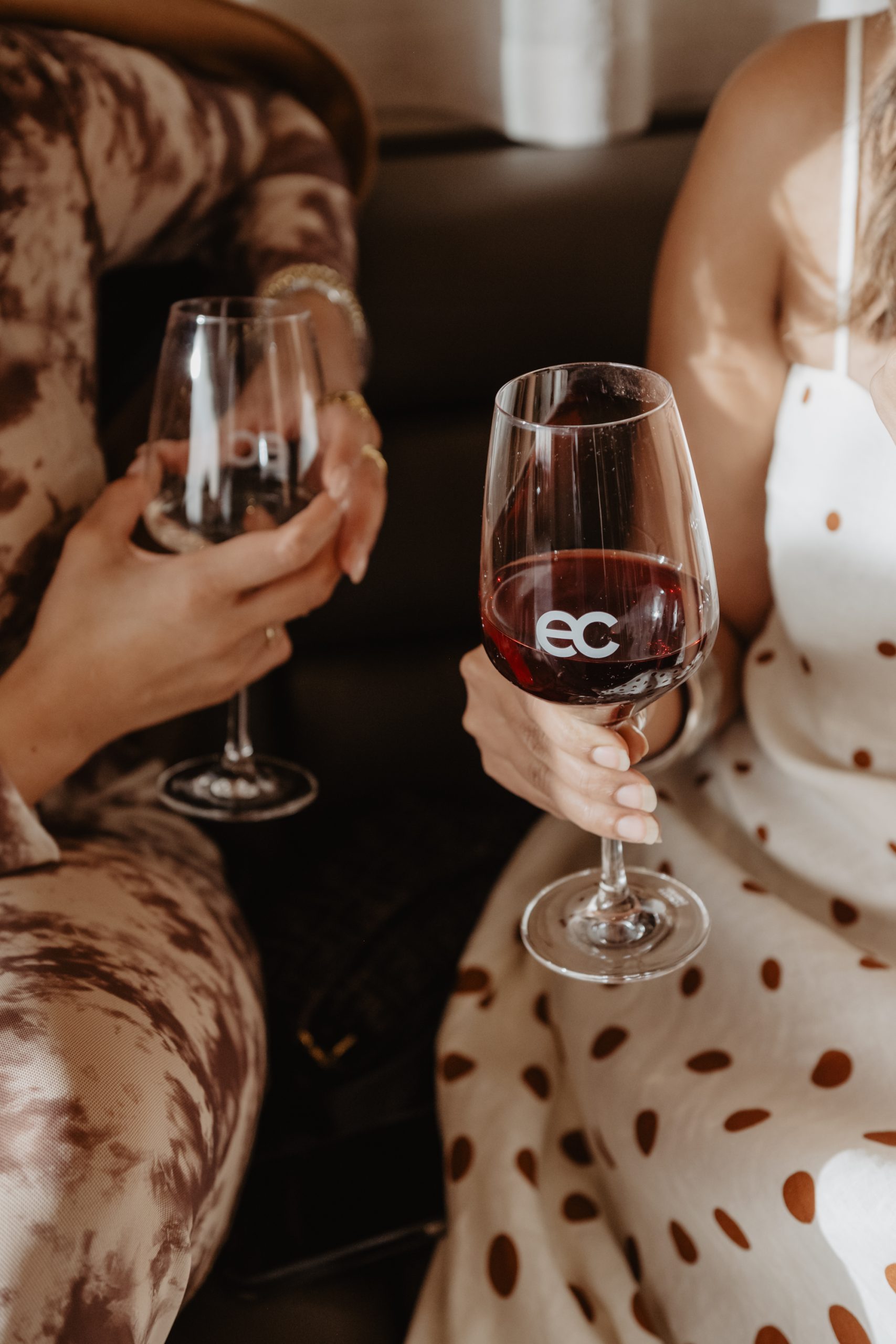 Close-up of two people clinking wine glasses, one glass etched with the eclat logo, at an event