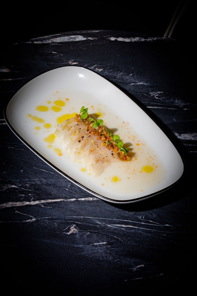 Delicately plated crudo drizzled with olive oil and garnished with microgreens on a white dish.