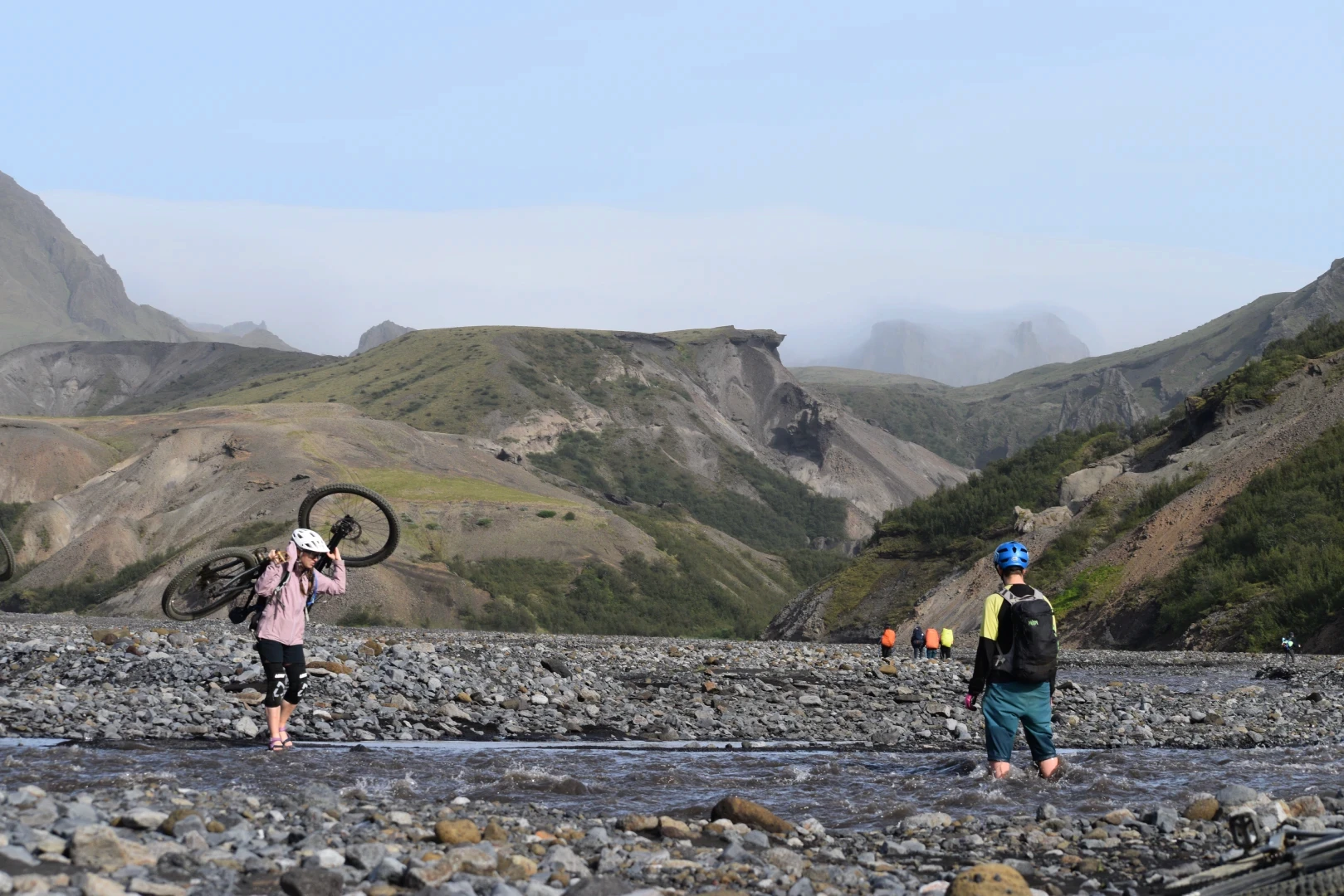 Two riders carry bike over a river in Iceland