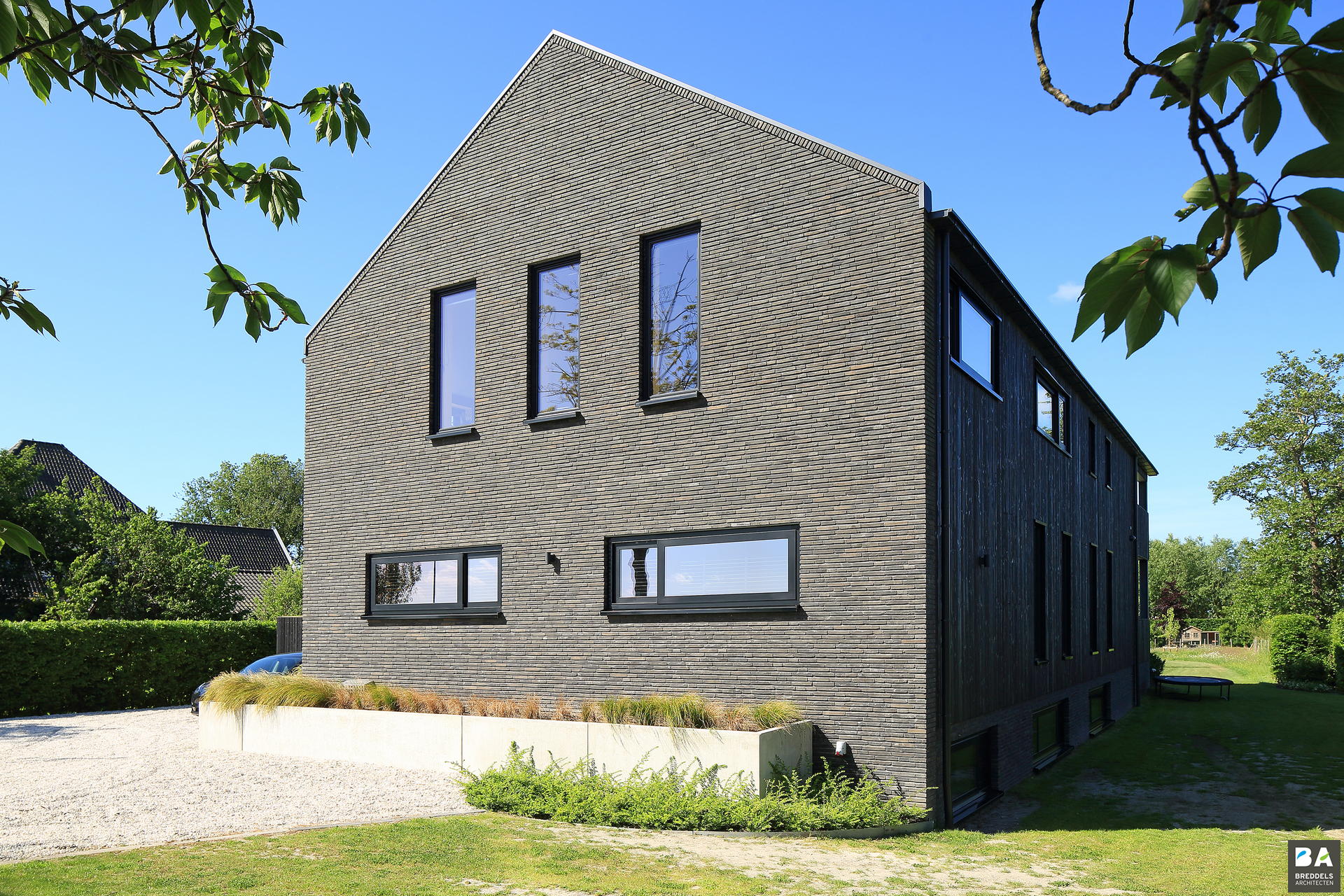 Moderne woning met grijze bakstenen en zwarte houten gevel onder blauwe lucht.