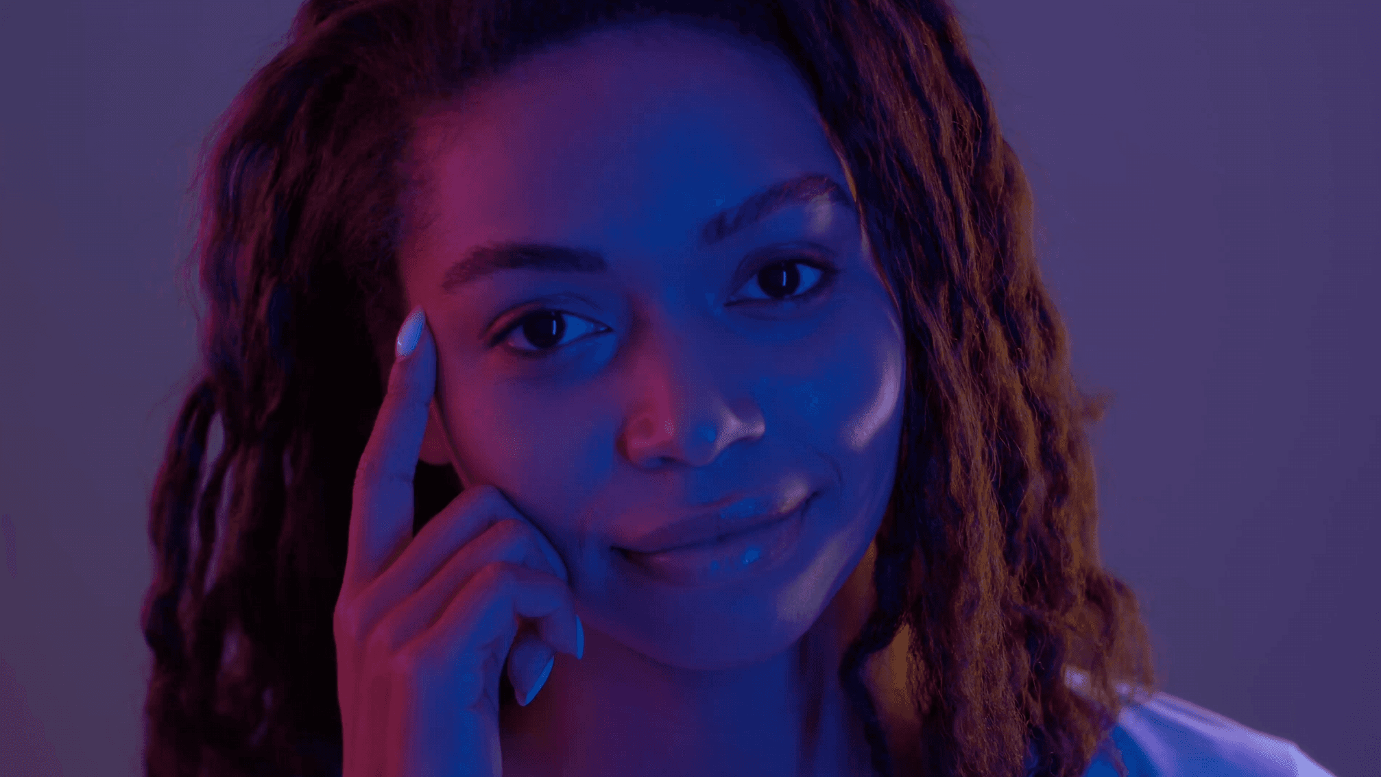Close-up portrait of woman touching her temple under blue and pink lighting