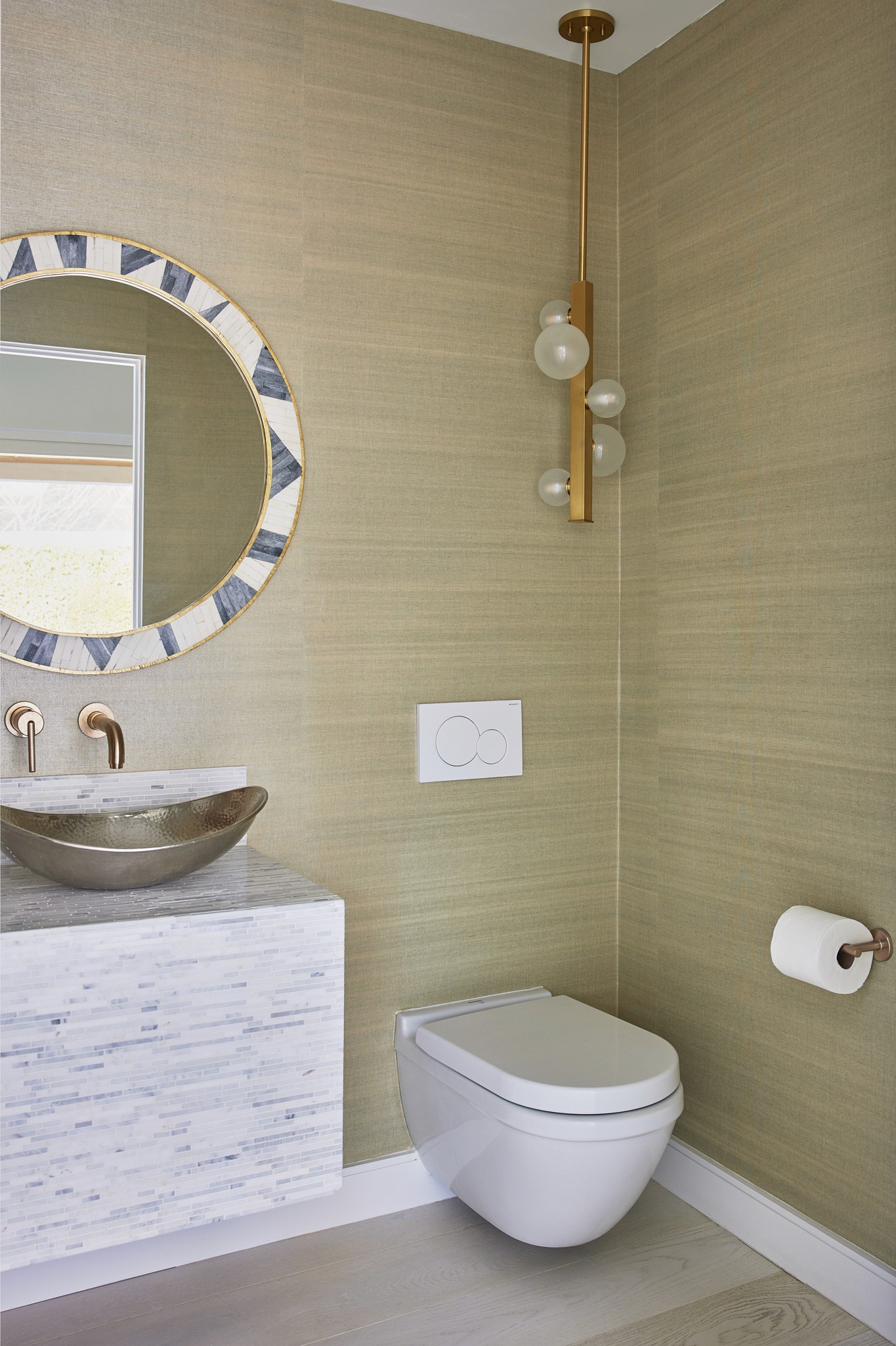 Powder bath with metal vessel sink, gold fixtures, round decorative mirror, bubble pendant light, and mosaic tile wall hung vanity by Jubilee Interiors in Los Angeles, California