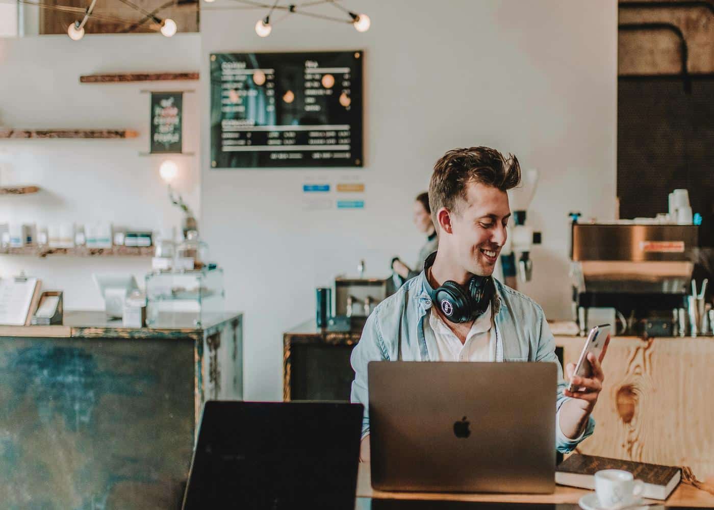 Man looking at phone smiling with a laptop in front of him