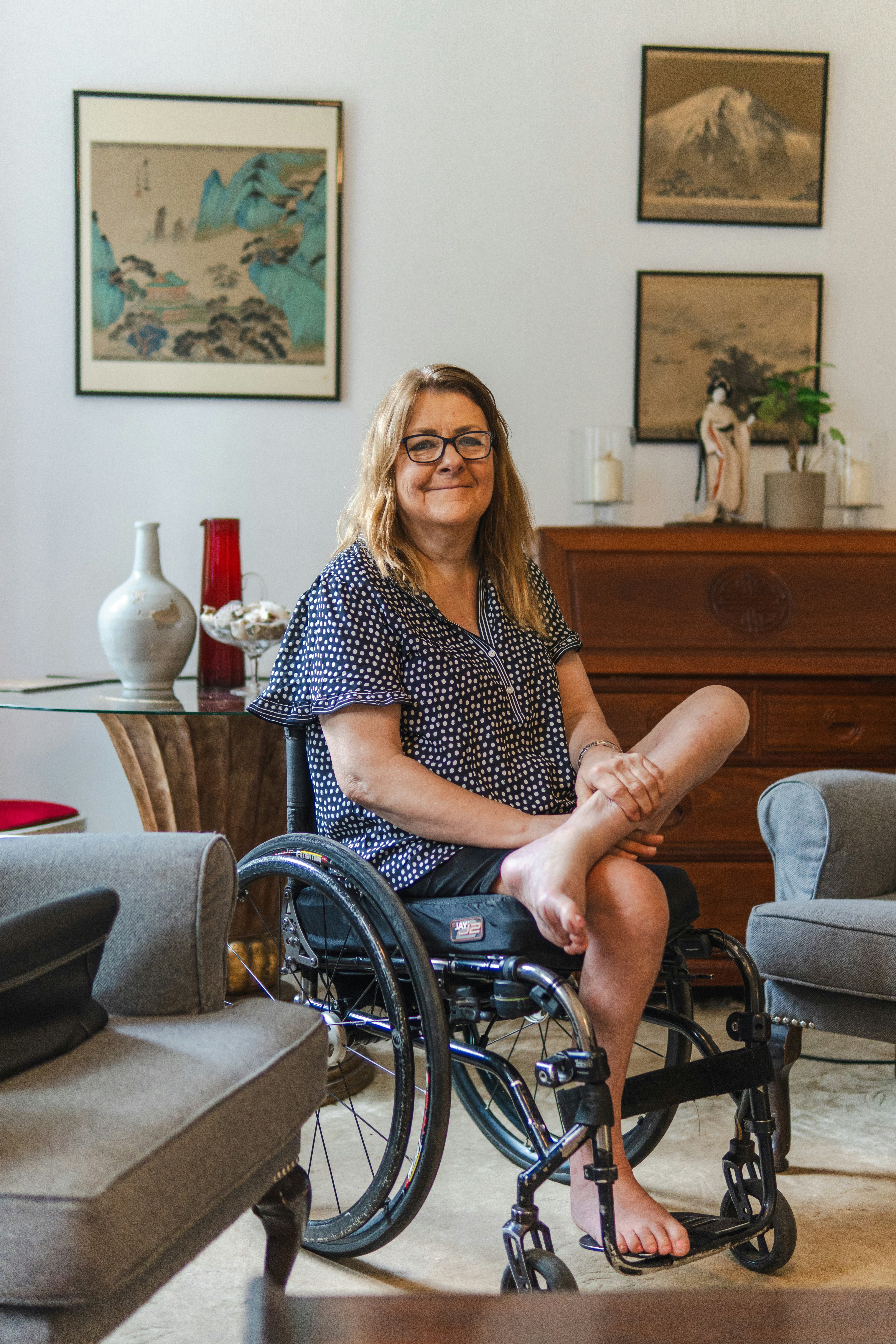 A woman smiles while sitting in a wheelchair indoors.
