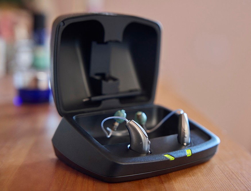 A black charging case displaying a pair of wireless earbuds, resting on a wooden surface.