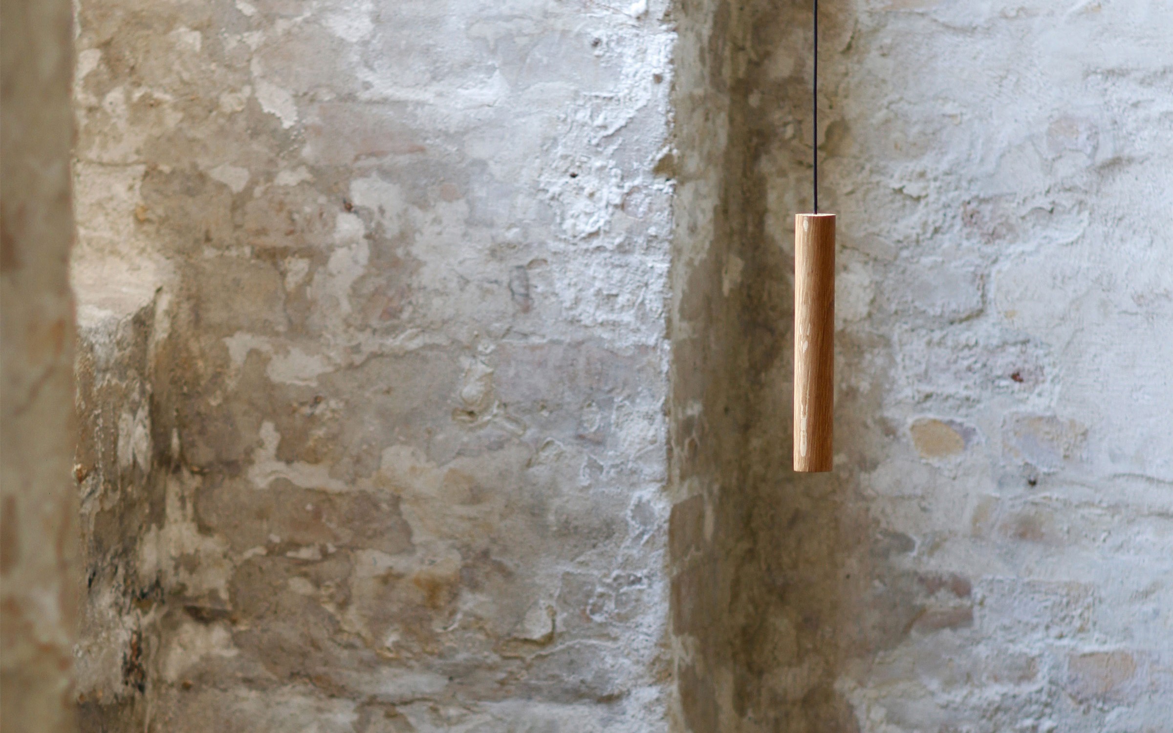 Chimes pendant lamp in solid oak suspended against textured brick wall designed by Asger Risborg Jakobsen