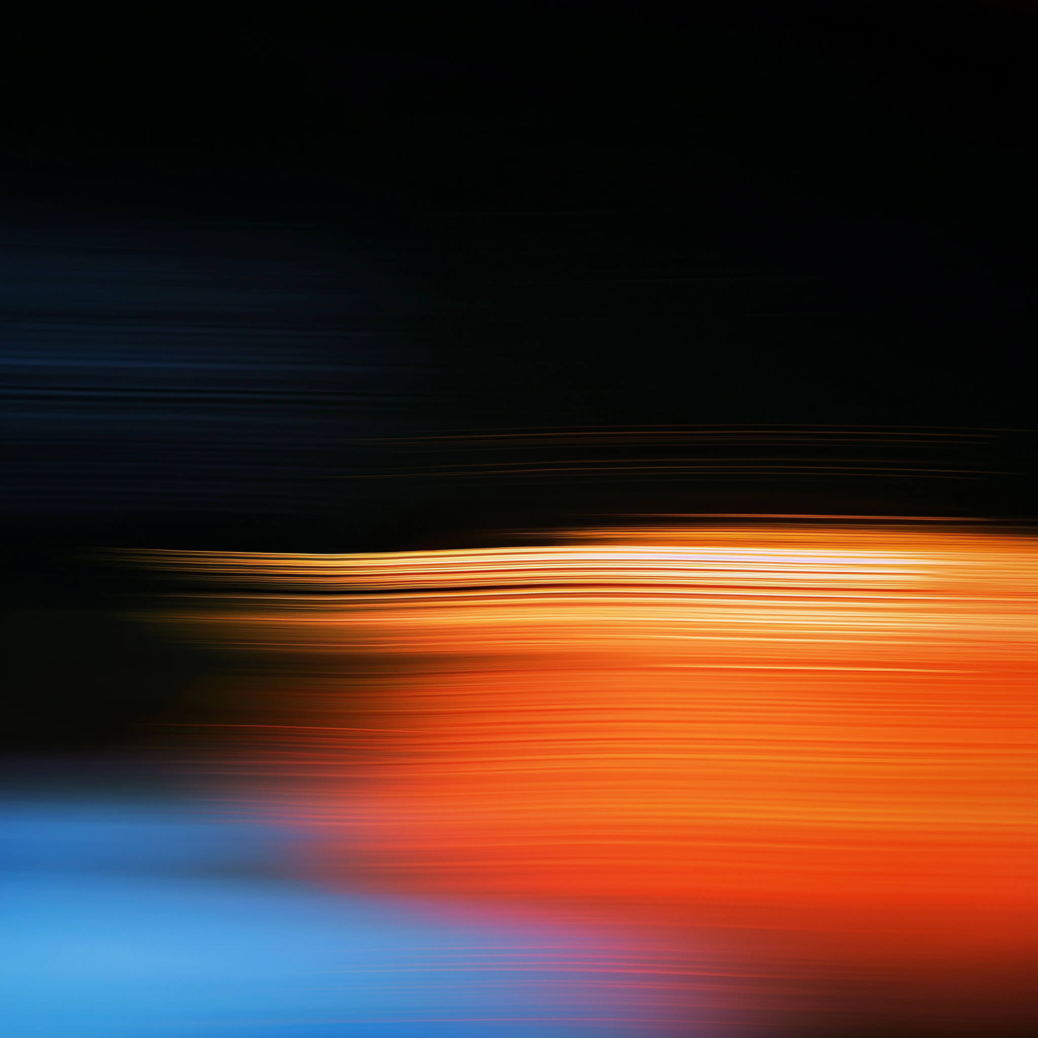 Abstract long-exposure light painting with horizontal streaks of orange, red and blue fading into a dark black background.