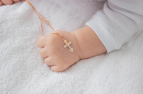 Collier de baptême posé sur une main de bébé.