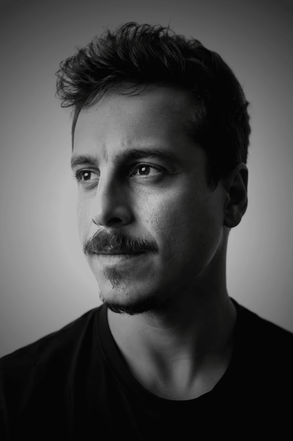 A thoughtful young person with dark hair gazes to the side, captured in soft black and white lighting.