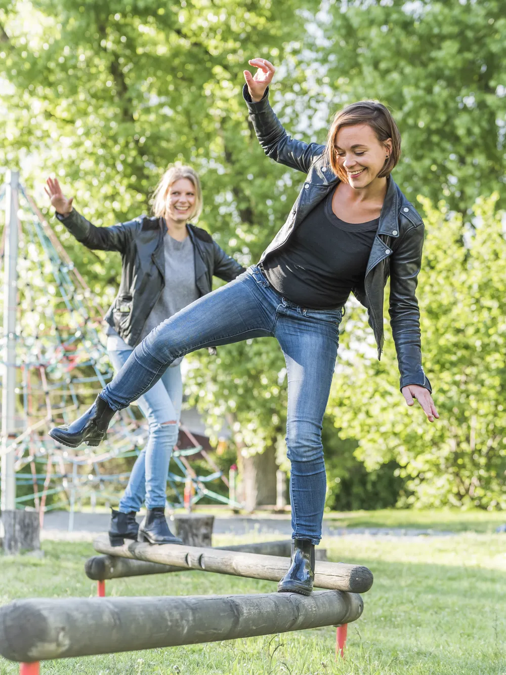two woman balancing on a log in a park