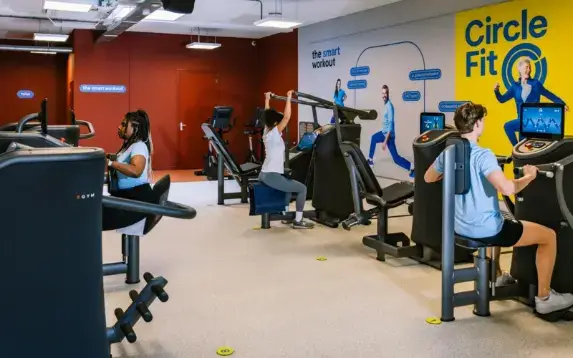 Two individuals are exercising on stationary bikes in a gym setting, focused on their workouts.