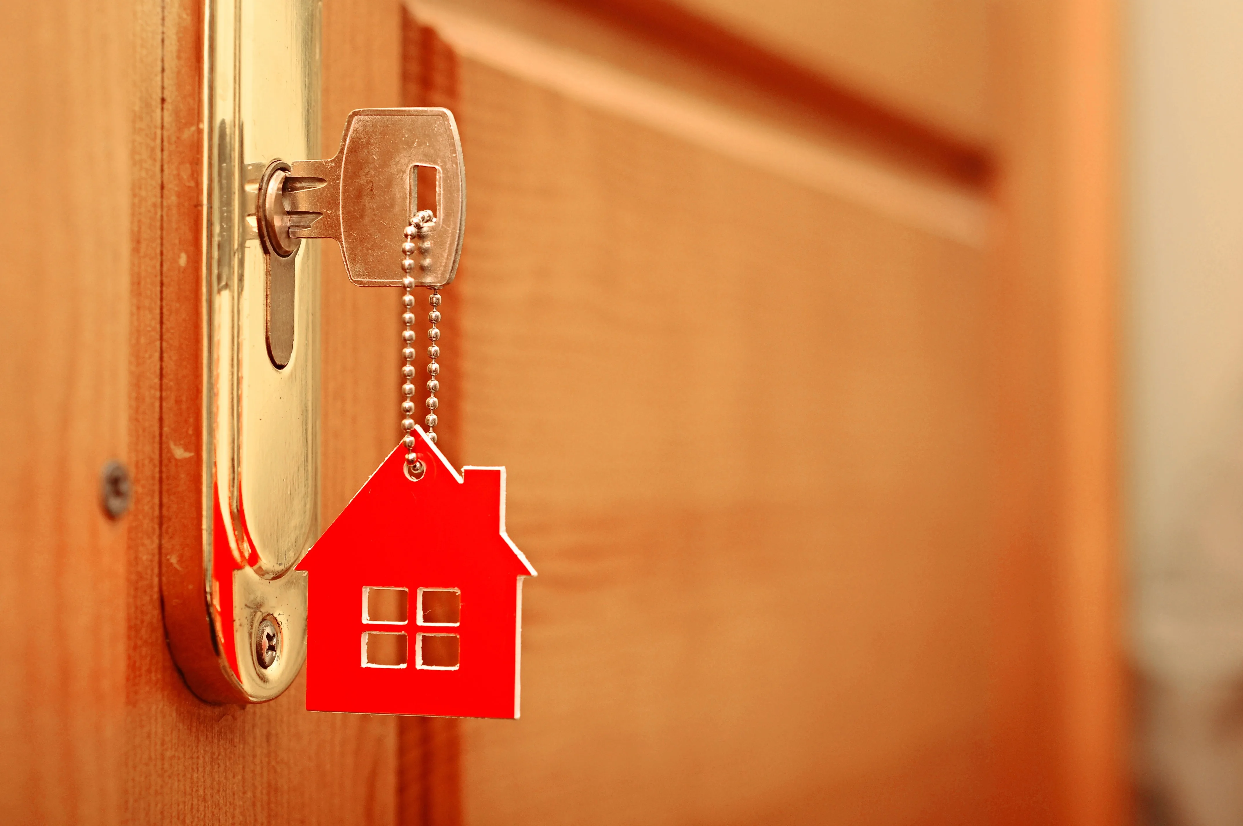 Key in door with a  keychain, in the shape of red house, hanging from it.