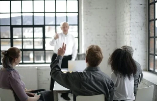 Team member raising a hand during a presentation or team meeting in a modern office setting.