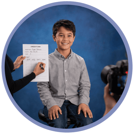 Traditional school picture day workflow showing a photography assistant holding a printed student order form and writing image numbers by hand while a student poses for a portrait and the photographer captures the session in a professional studio.