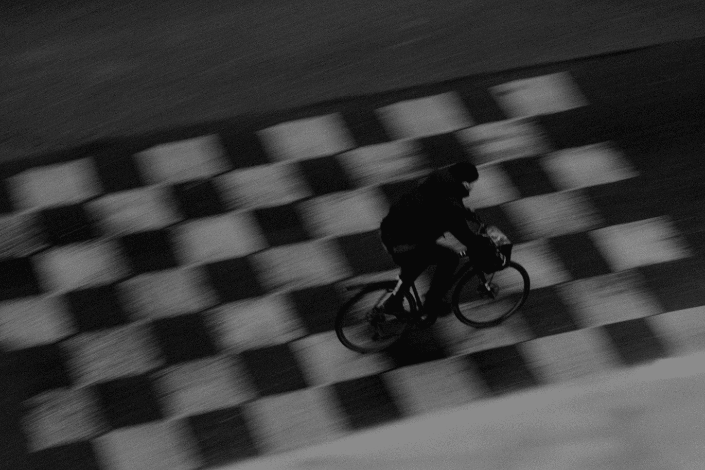 Black-and-white image of a cyclist in motion, captured with motion blur against a patterned track