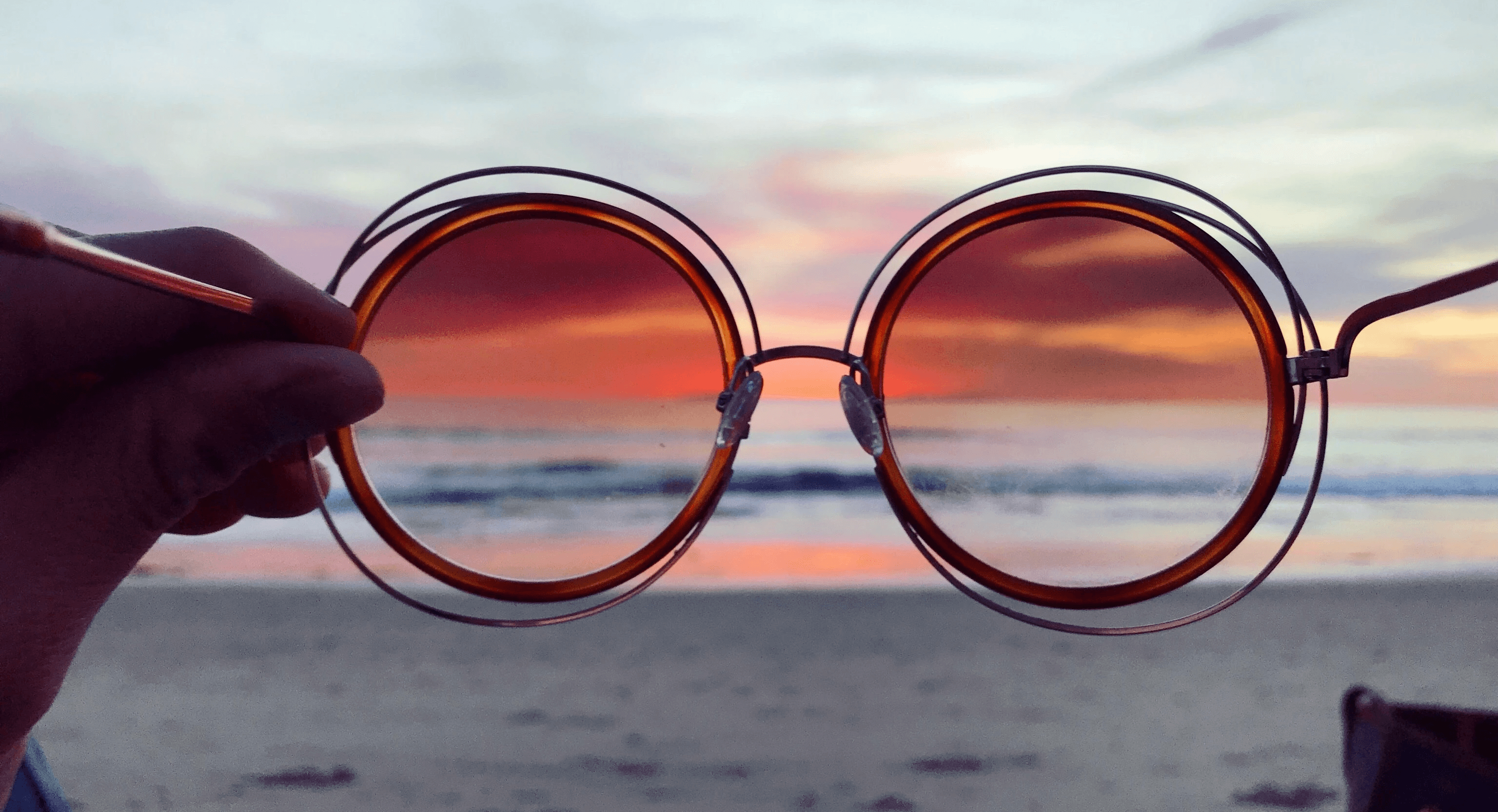 a person holding up a pair of sunglasses on the beach