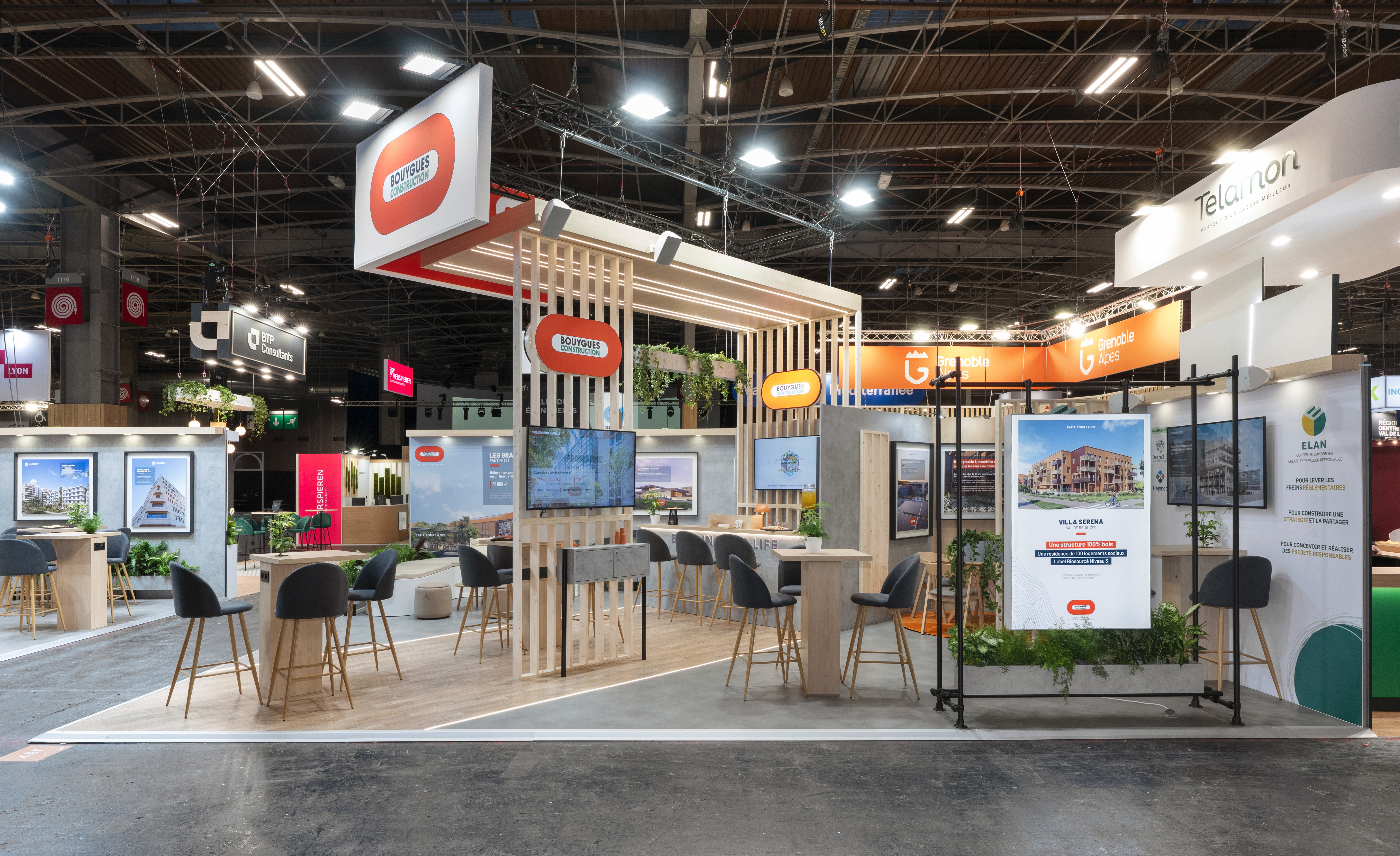 Stand Groupe Bouygues salon SIMI 2025 Paris réalisé par Expace – vue frontale avec structure orange et blanche, caisson suspendu et espace lounge design ouvert