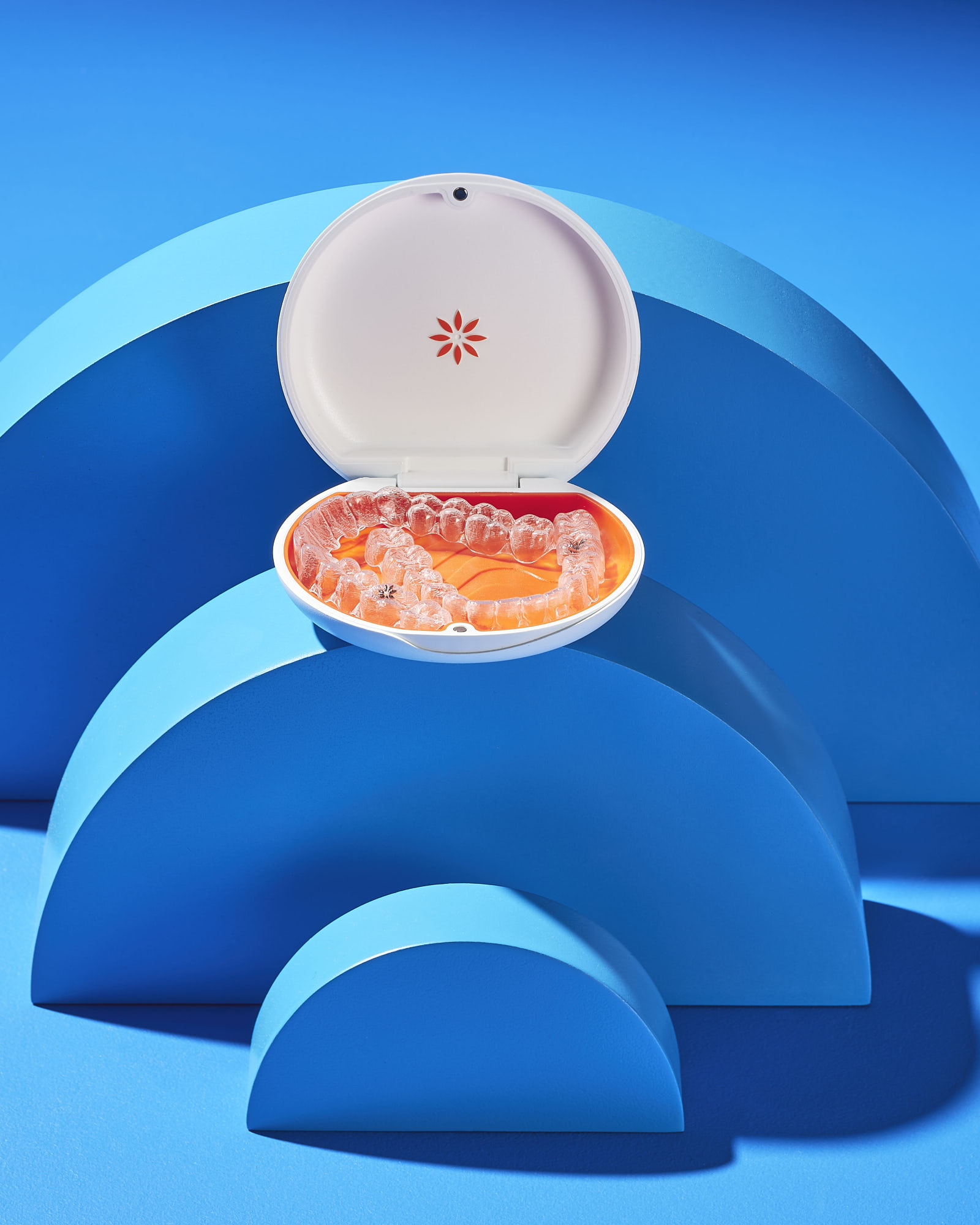 Clear dental aligner in a white case on a blue artistic background.