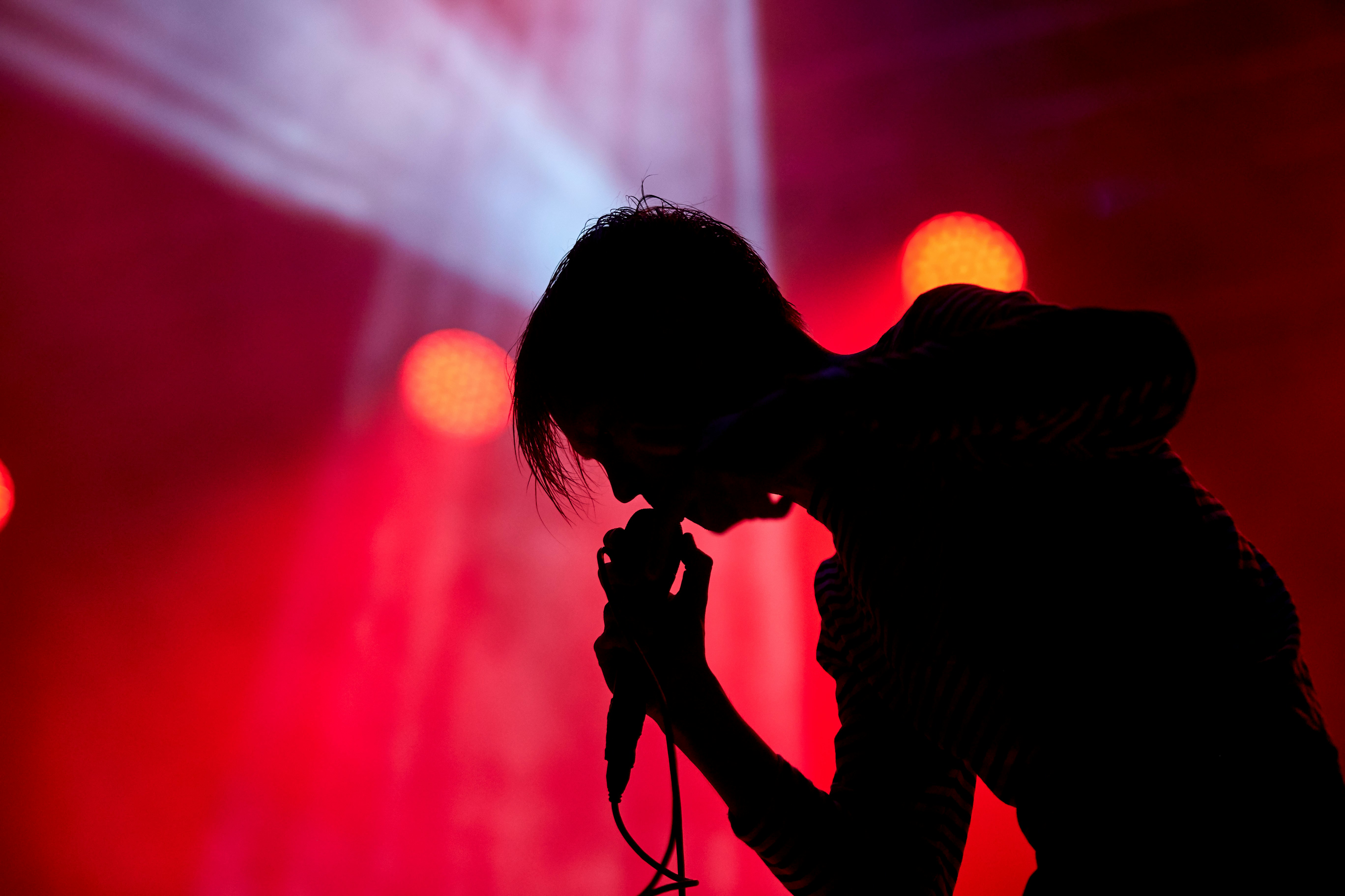 Silhouette of a male vocalist singing while leaning against mic on stage. Photo by Angel Arcalle on Unsplash