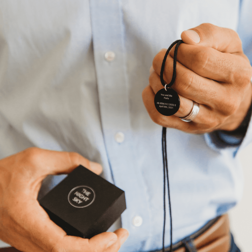 A man holding a Black Onyx Night Sky Star Map pendant on one hand and a black jewellery box on the other one. 