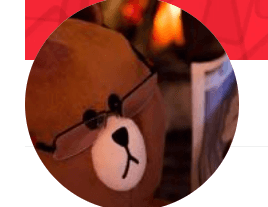 The image shows a plush brown bear wearing glasses, appearing to read something, with warm lighting in the background, creating a cozy vibe.