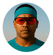 Man in a teal headband and shirt wearing orange-tinted glasses, looking forward with a serious expression.