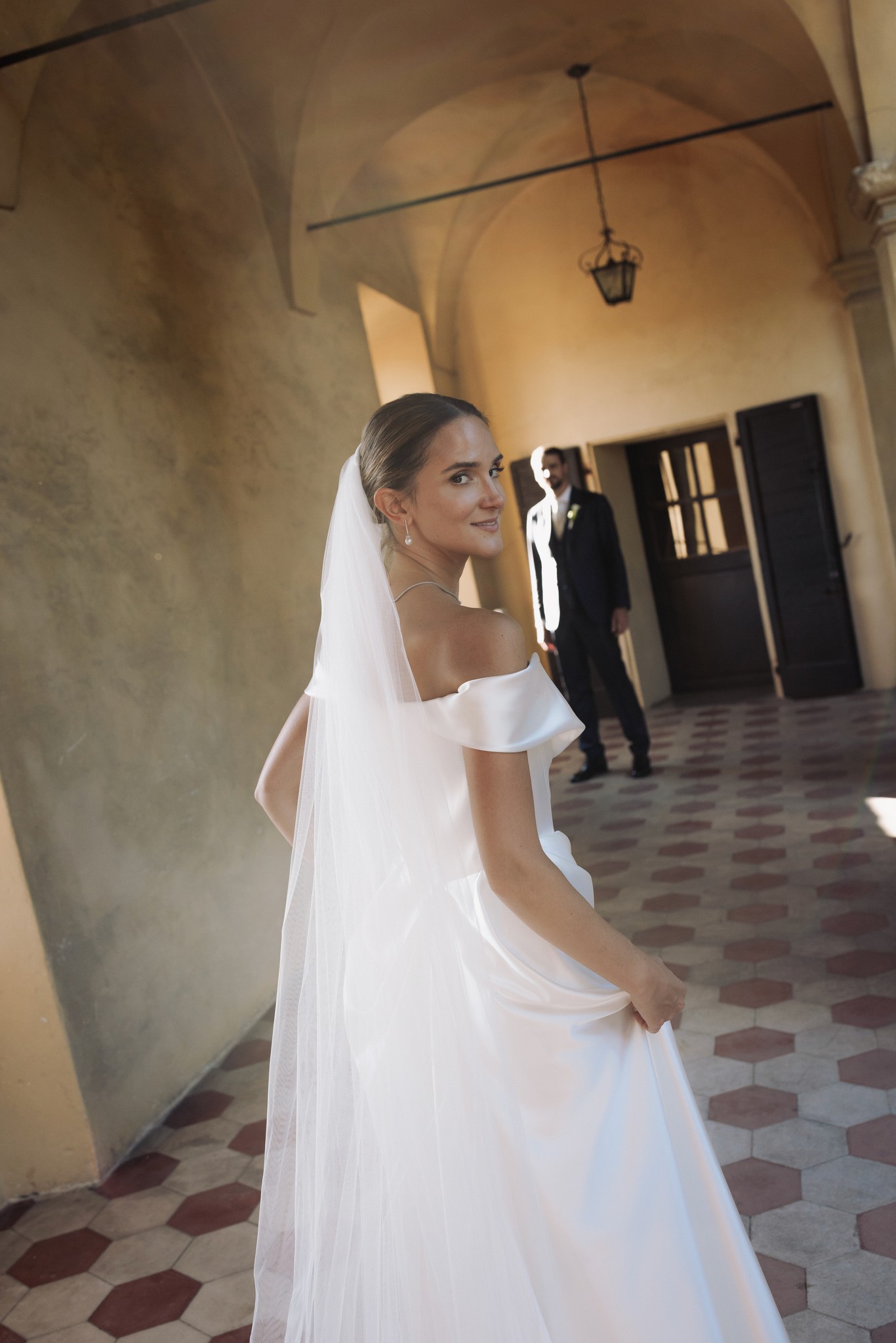 Sposa in abito bianco nel corridoio del Castello di Scipione, velo lungo, luce naturale sull'architettura medievale