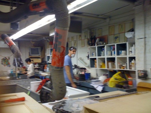 A photo of two people wearing masks while working in a woodworking workshop.