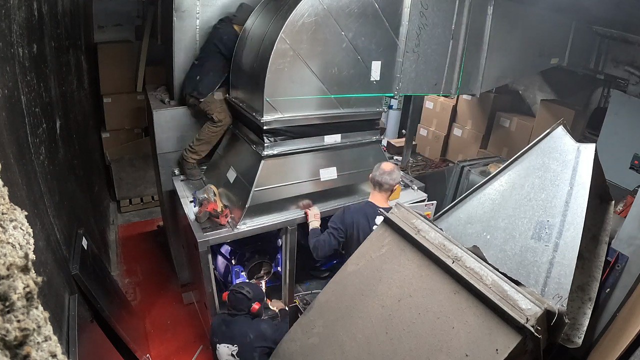 Technicians fitting duct transition on new return fan assembly during install.