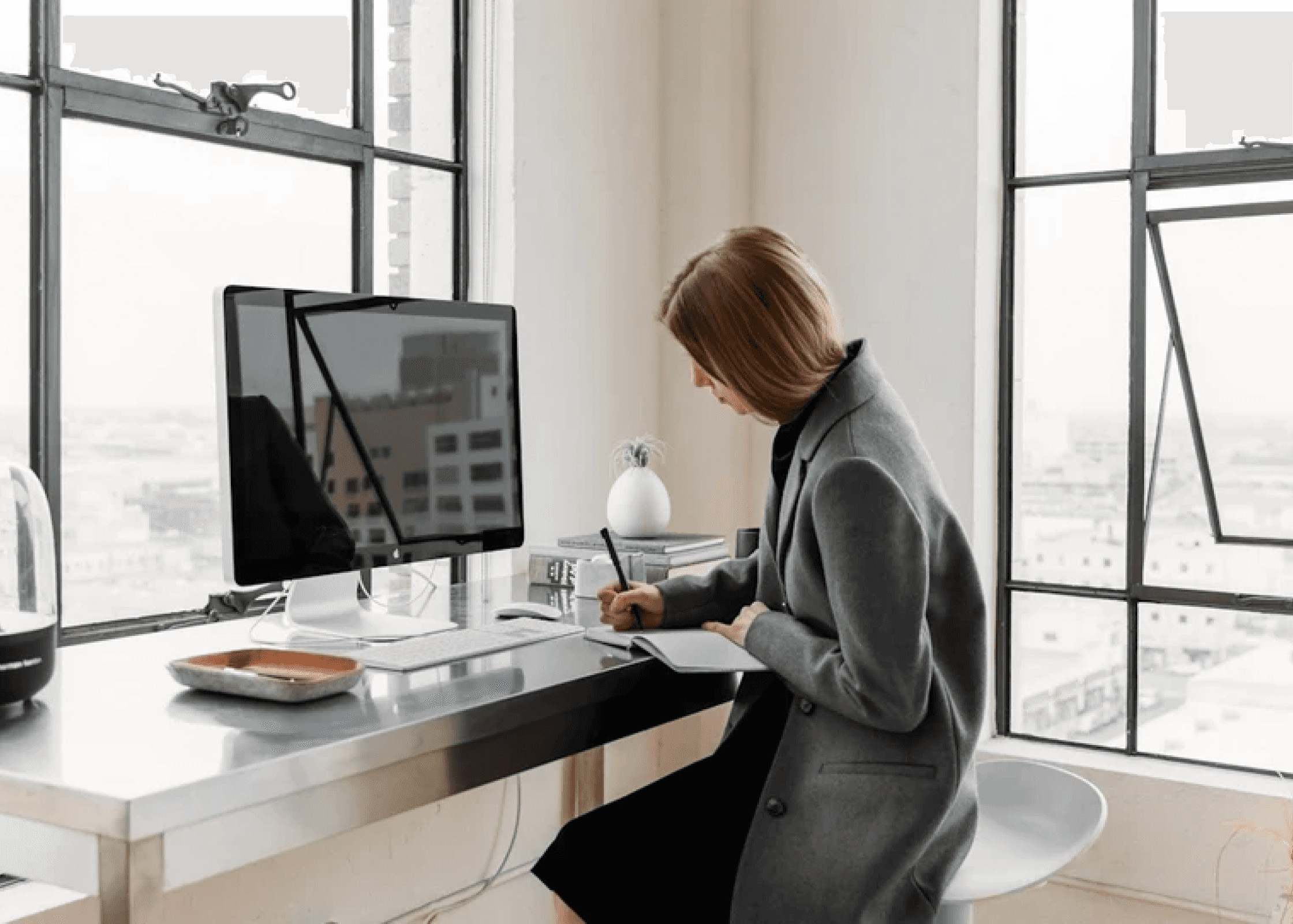 A woman seated at a desk, focused on her computer while holding a pen in her right hand