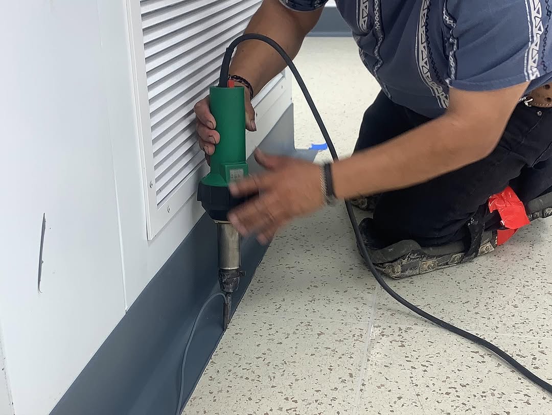 Installer heat-welding cove base against an equipment room wall