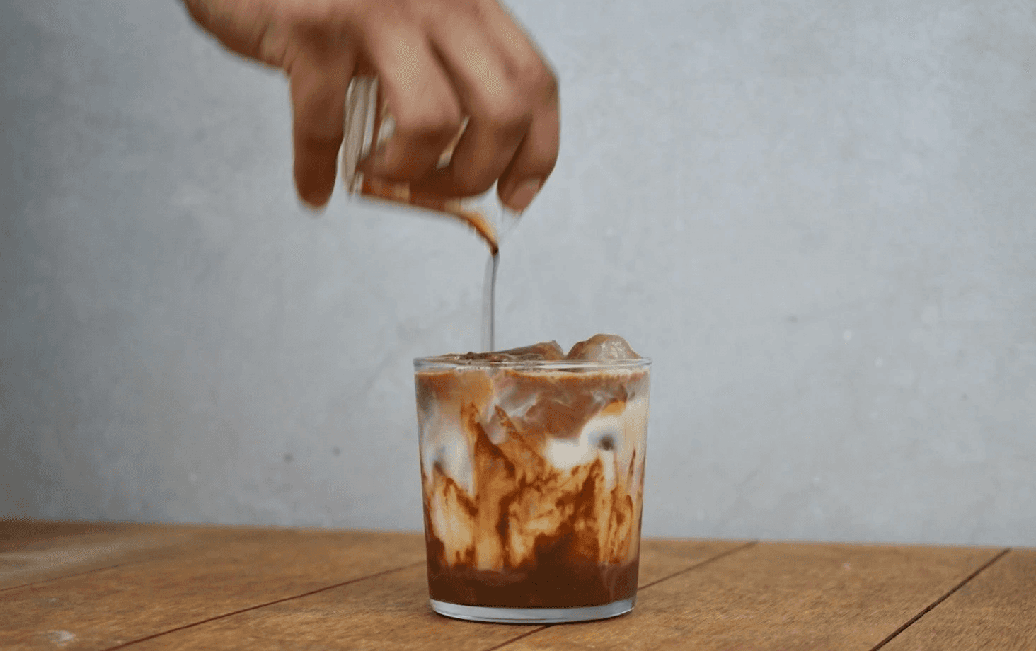 Close-up portrait of a model with pastel pink buzz-cut hair, soft pink eyeshadow, and multiple facial piercings, set against a vibrant green background.