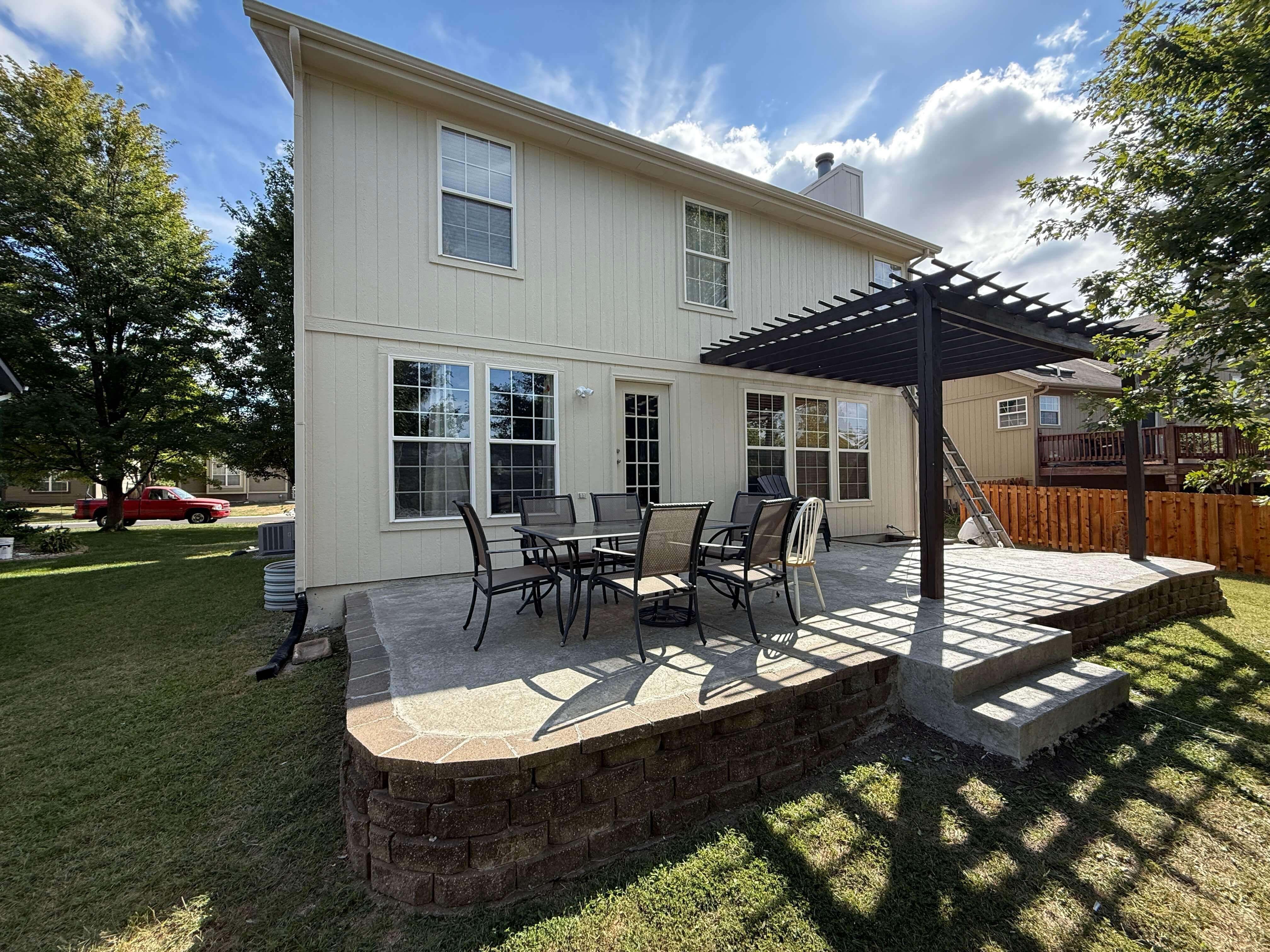 An image showing a concrete and stone patio with a pergola and patio dining furniture.