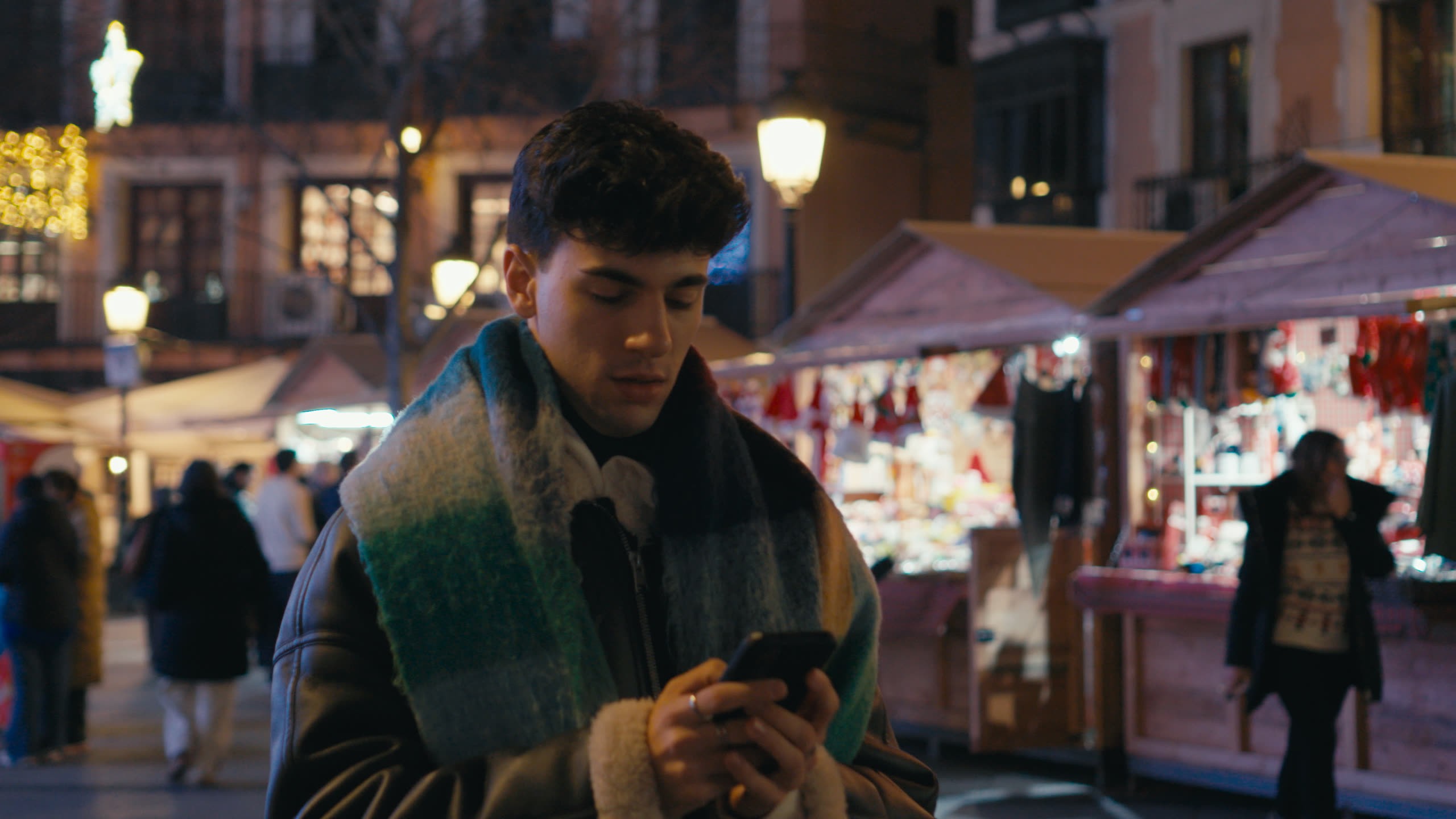 Un joven mira el móvil entre los puestos iluminados del mercado navideño de Toledo