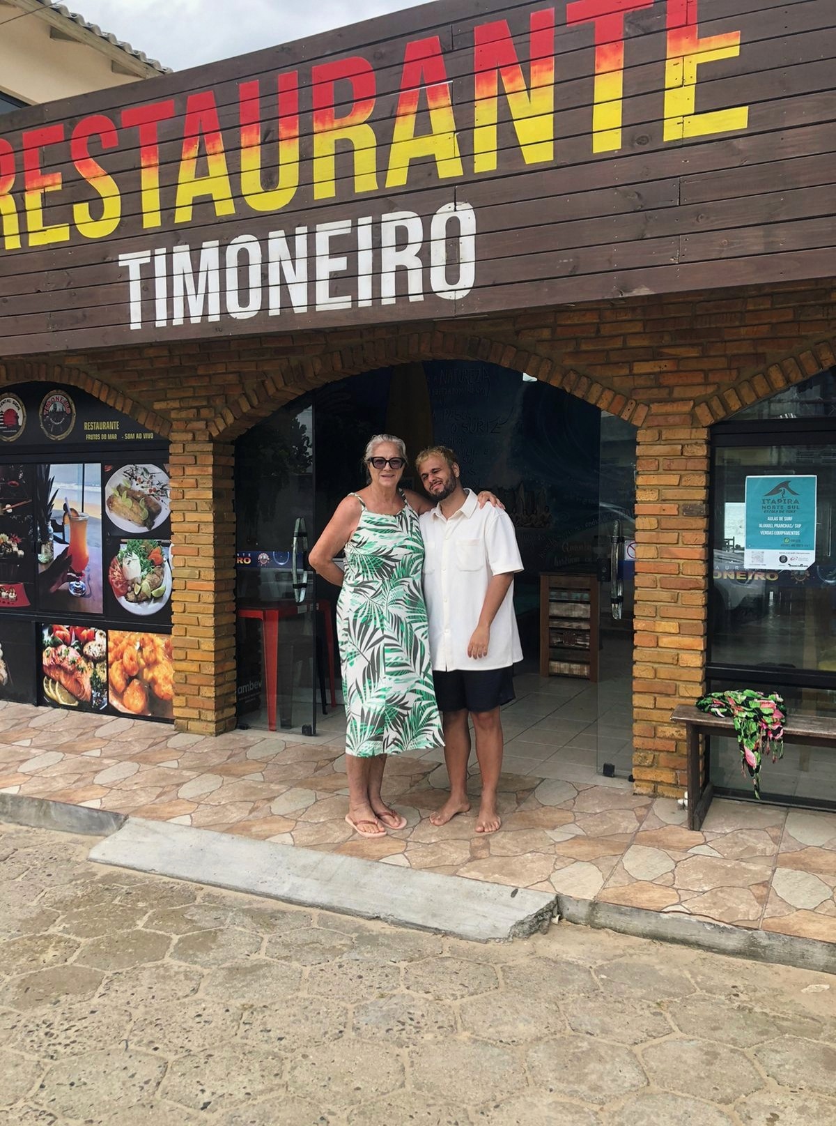 A view from an airplane window shows the aircraft's wing with a golden hue reflecting the setting sun, against a serene backdrop of fluffy clouds and a clear sky.