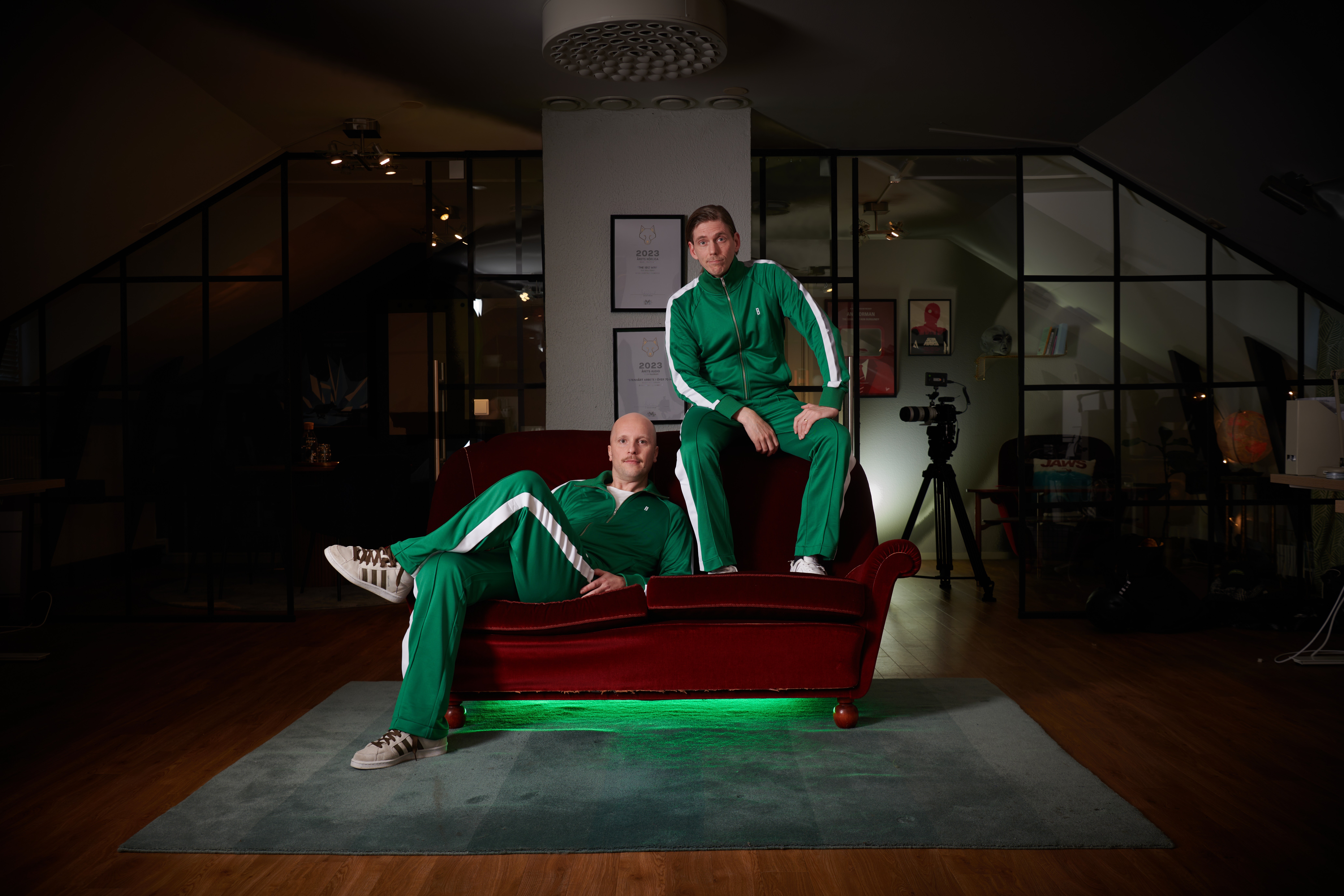 Two persons sitting on a couch in a room looking fly in green jump suites
