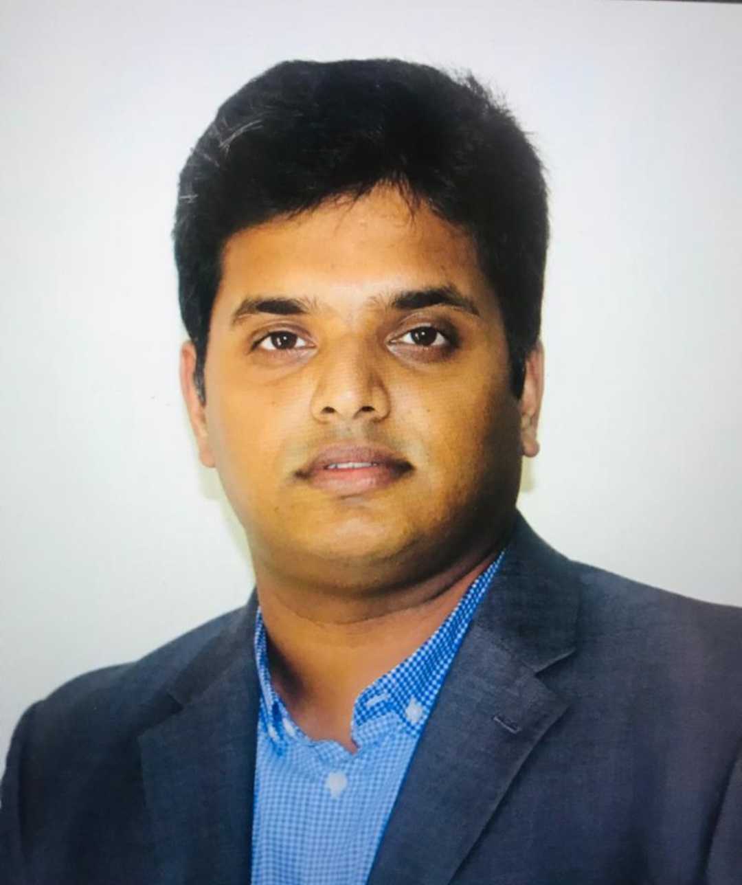 Man with a beard in a dark button-up shirt, smiling while writing in a notebook.