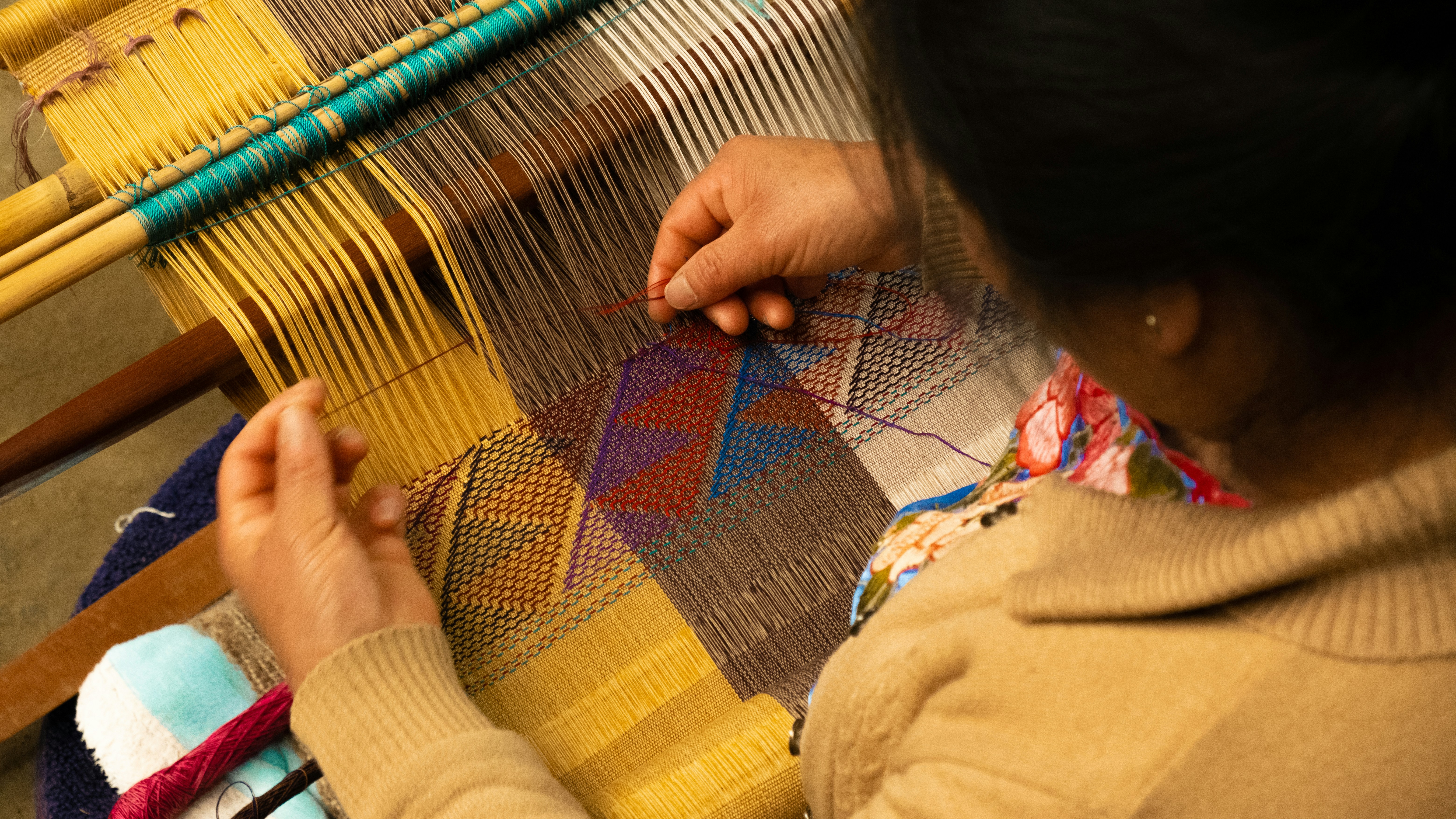 Person working on an intricate fabric pattern on a loom