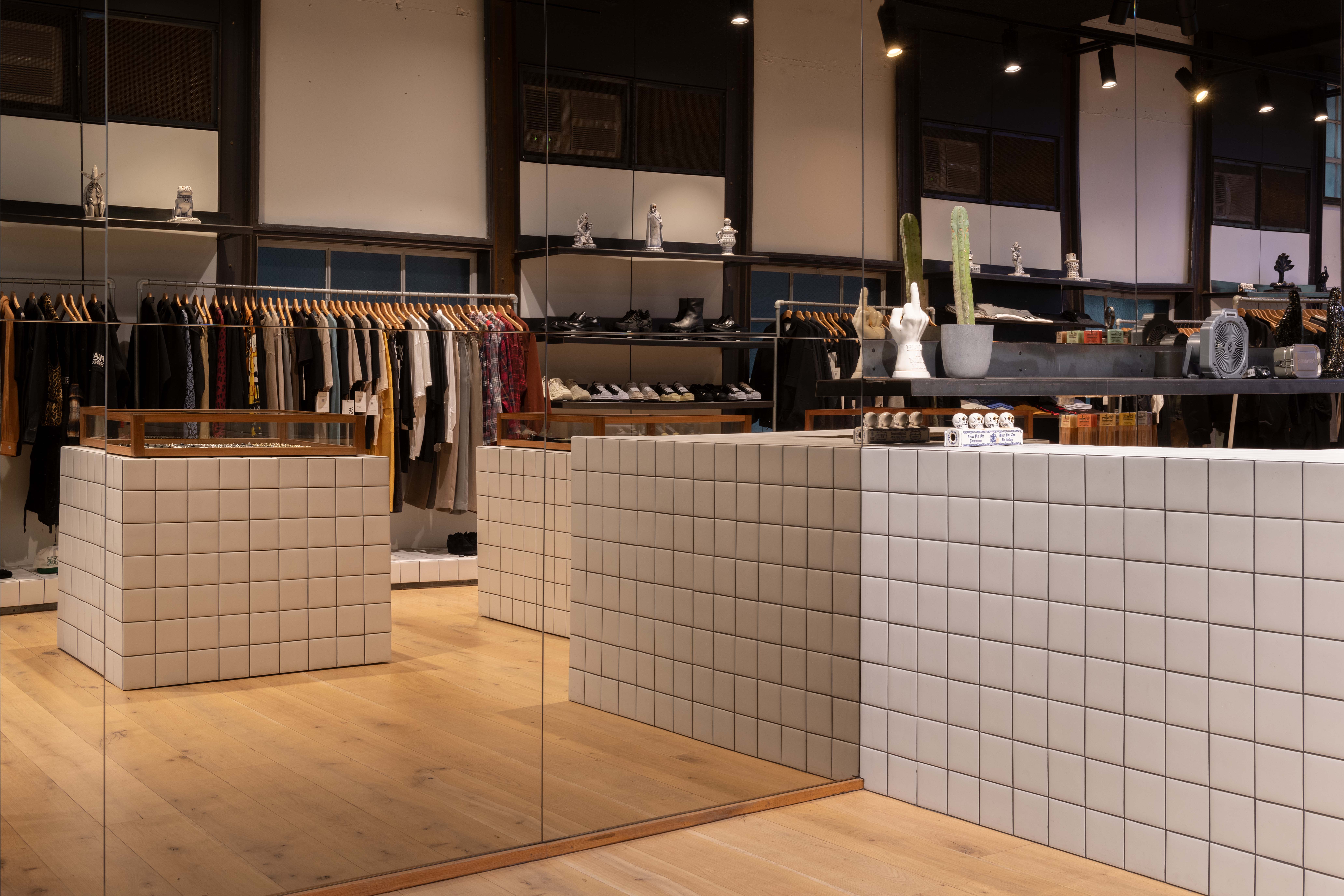 Mirrored interior detail of the 199A® store, featuring tiled modular display blocks, wall-length clothing racks, open shelving, and warm timber flooring under track lighting.