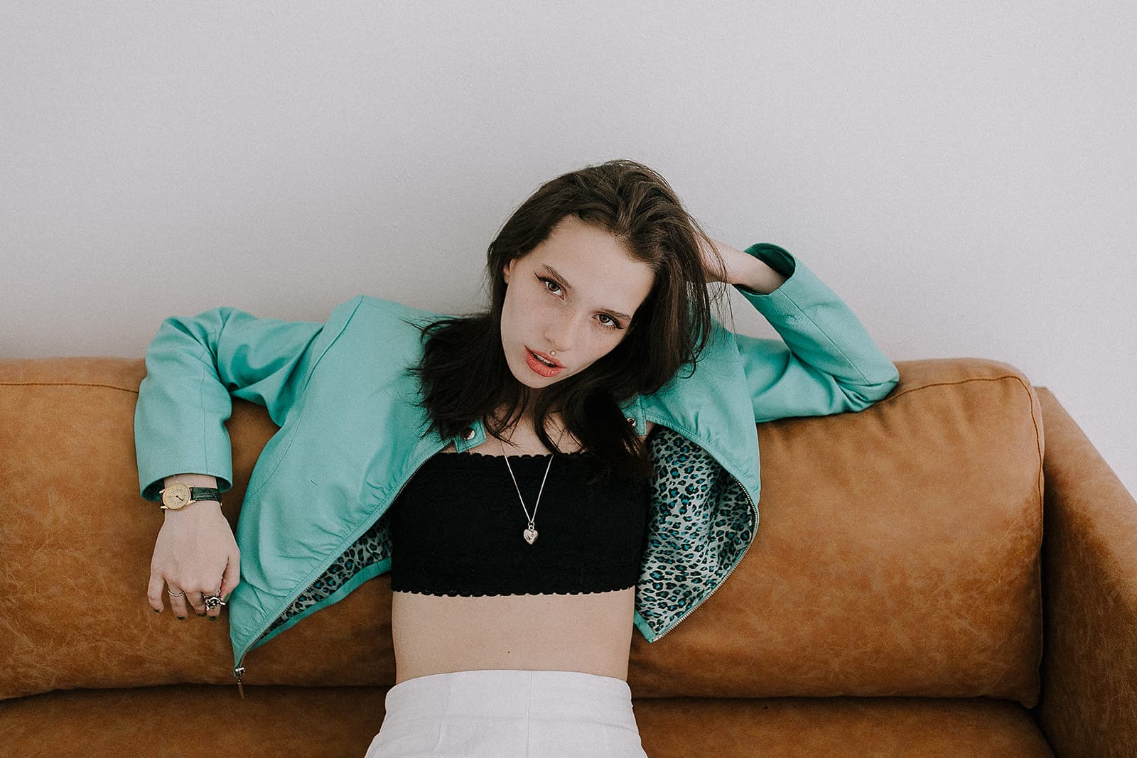 Model in teal jacket lounges on a brown sofa at Revelator Studio in Shreveport during a 90s fashion photoshoot.