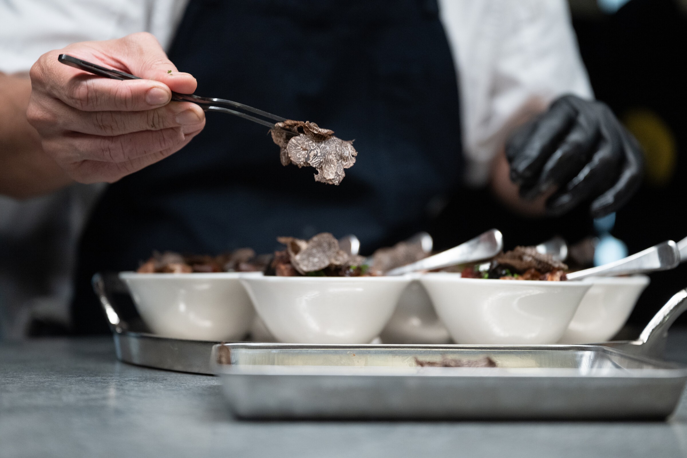 Full tweezers holding a slice of black truffle above plated dishes