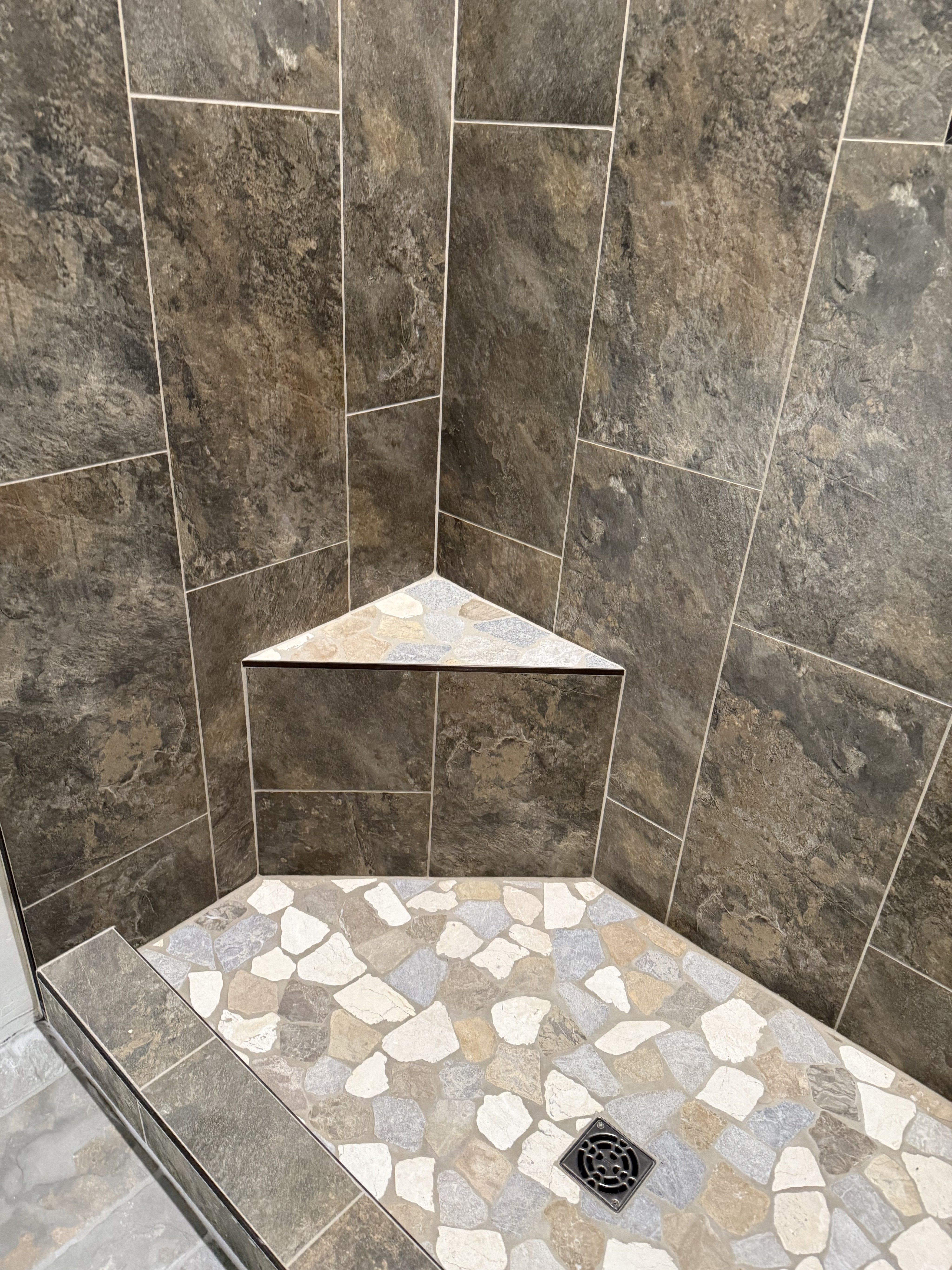 Contemporary bathroom featuring a large walk-in shower with white marble-look wall tiles and a black and white patterned mosaic shower floor, complemented by black hexagonal floor tiles throughout the bathroom.